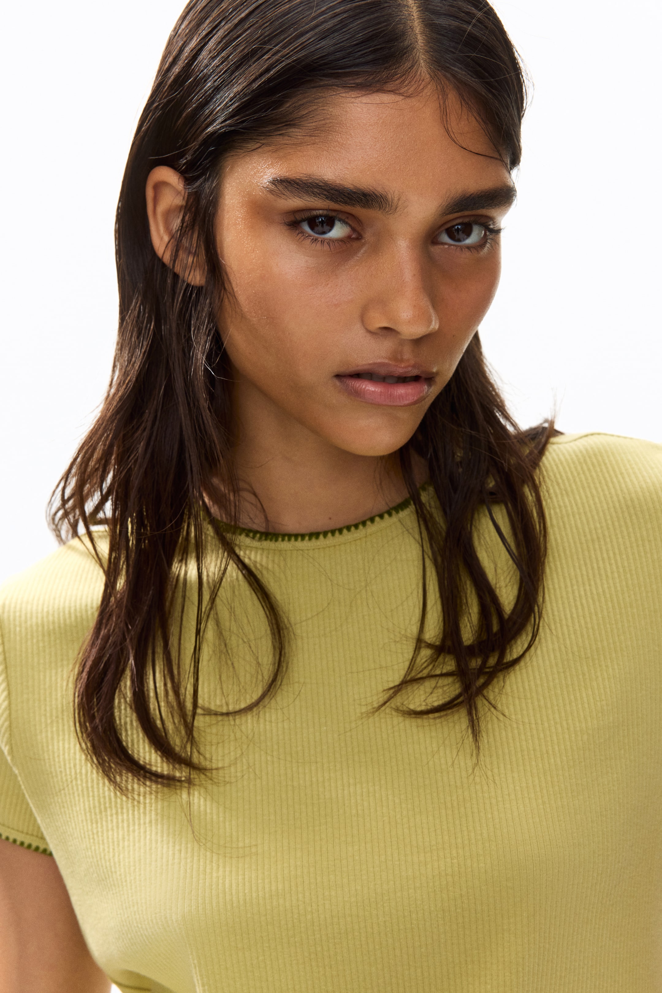 View larger image: The model is wearing a light green ribbed jersey T-shirt, highlighted by closed blanket stitching along its round neckline.