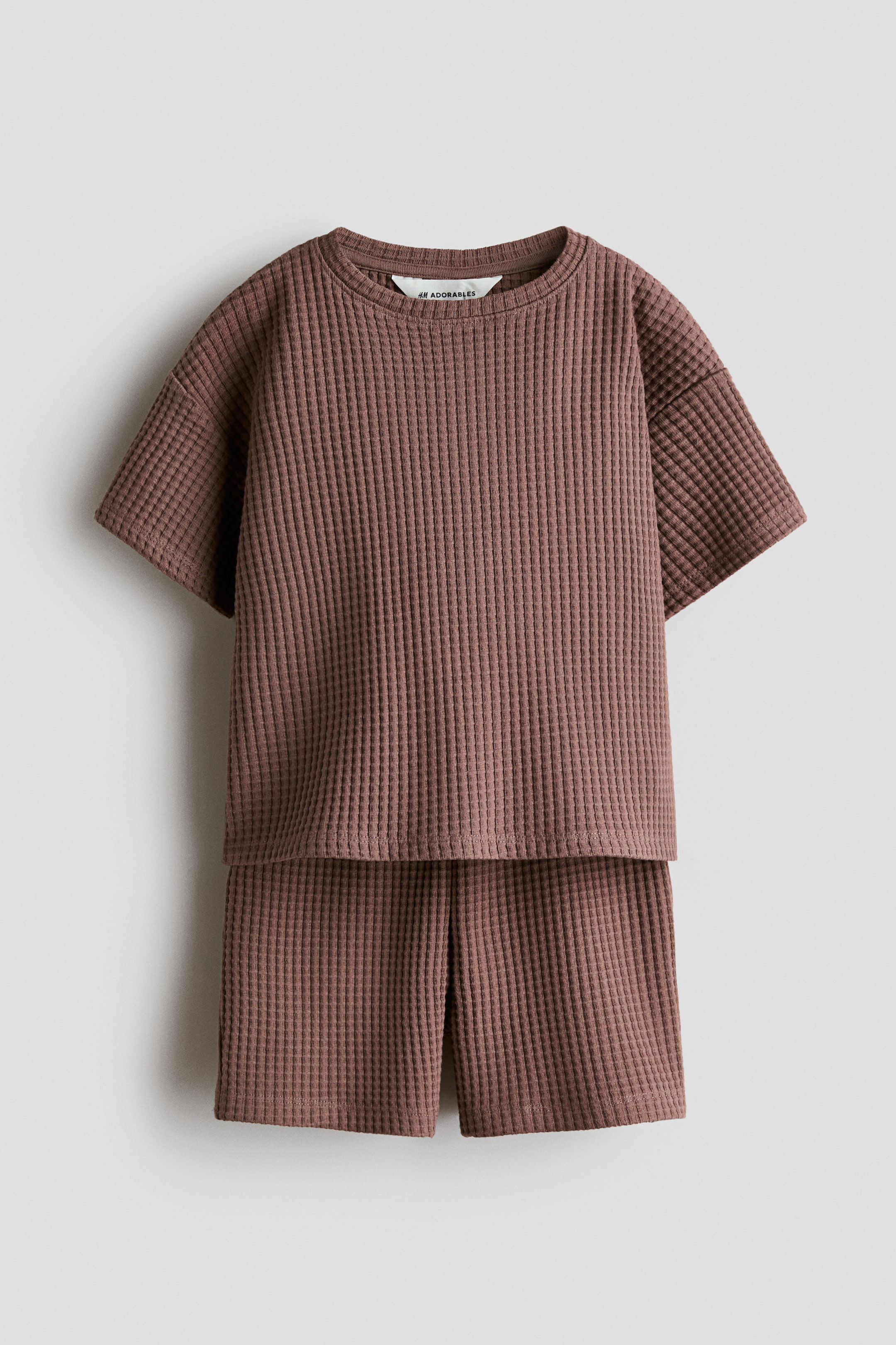 View larger image: The H&M Adorables set showcases a brown waffled jersey t-shirt and matching mid-thigh shorts, displayed front-facing. The t-shirt features a round neckline, low dropped shoulders, and a visible "H&M Adorables" label, while the shorts are designed with an elasticated waist.
