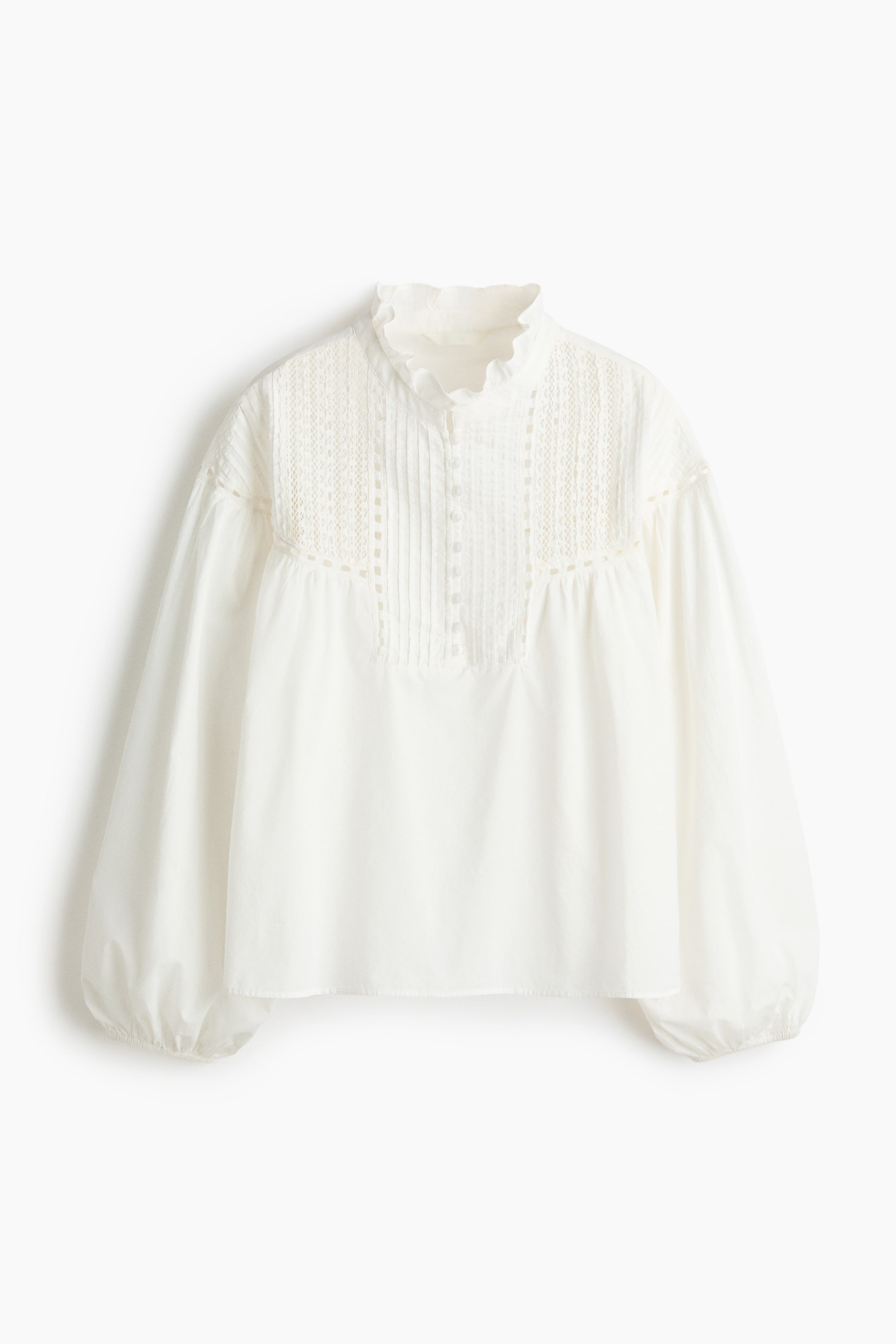 Agrandir l'image: Cette blouse blanche présente un col montant à volants et un empiècement avant orné de plis nervurés verticaux et d'inserts en dentelle horizontaux. Elle est conçue avec de longues manches volumineuses se resserrant dans des poignets élastiqués.