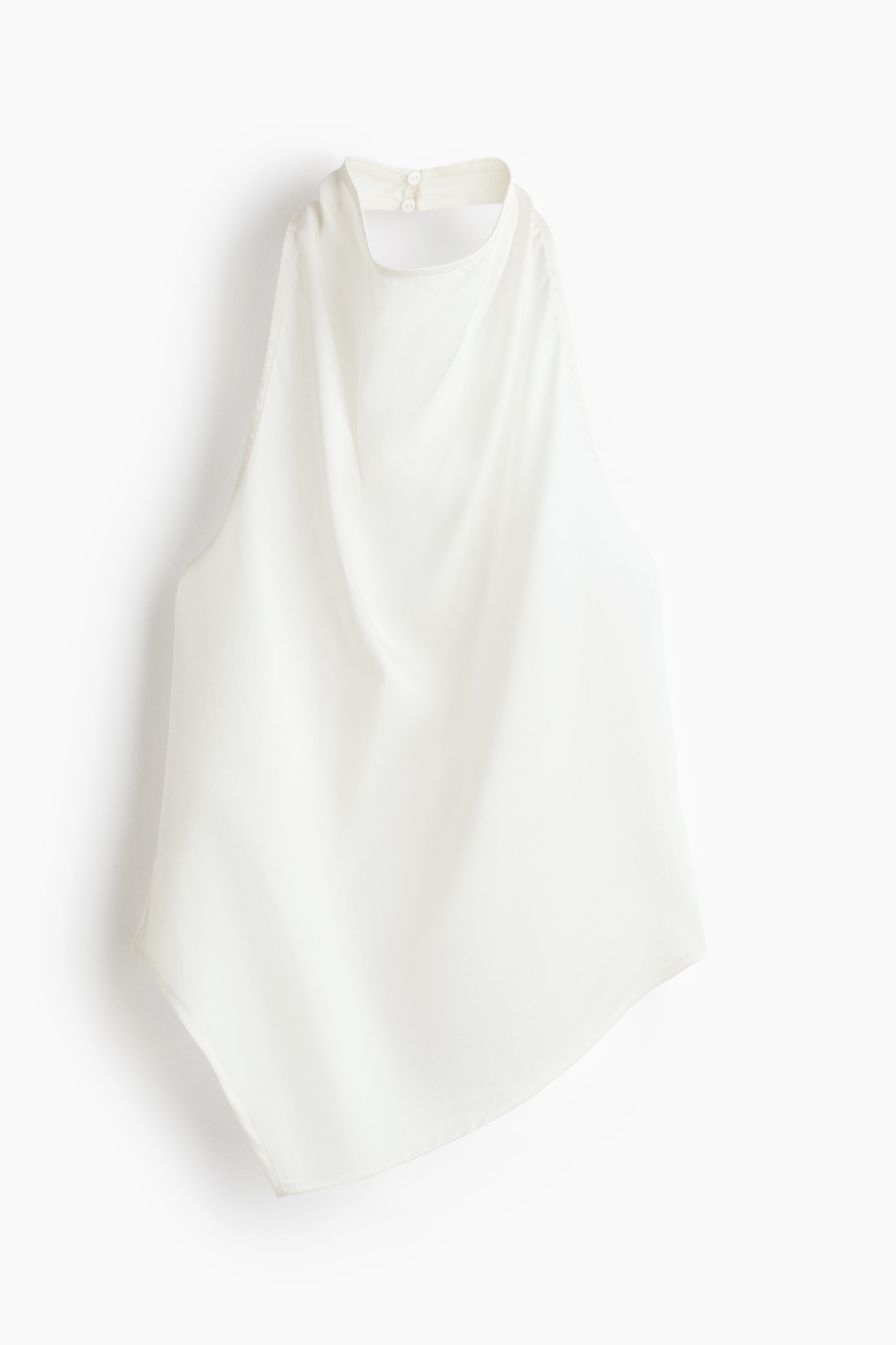 View larger image: "A cream halterneck top is showcased from the front, boasting a cowl neckline and an asymmetric hem. Crafted from a lyocell weave with a gentle sheen, it features two buttons visible at the back of the neck."