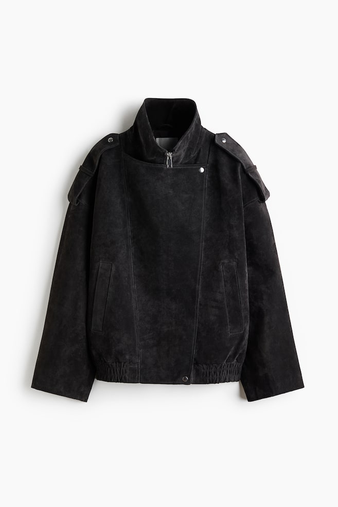 A black suede jacket is facing front, featuring a high collar with a partial zipper and an asymmetrical overlay panel with snap-button closures. The jacket is displaying dropped shoulders with snap-button epaulets, vertical side welt pockets, and a gathered elastic hem. - 1