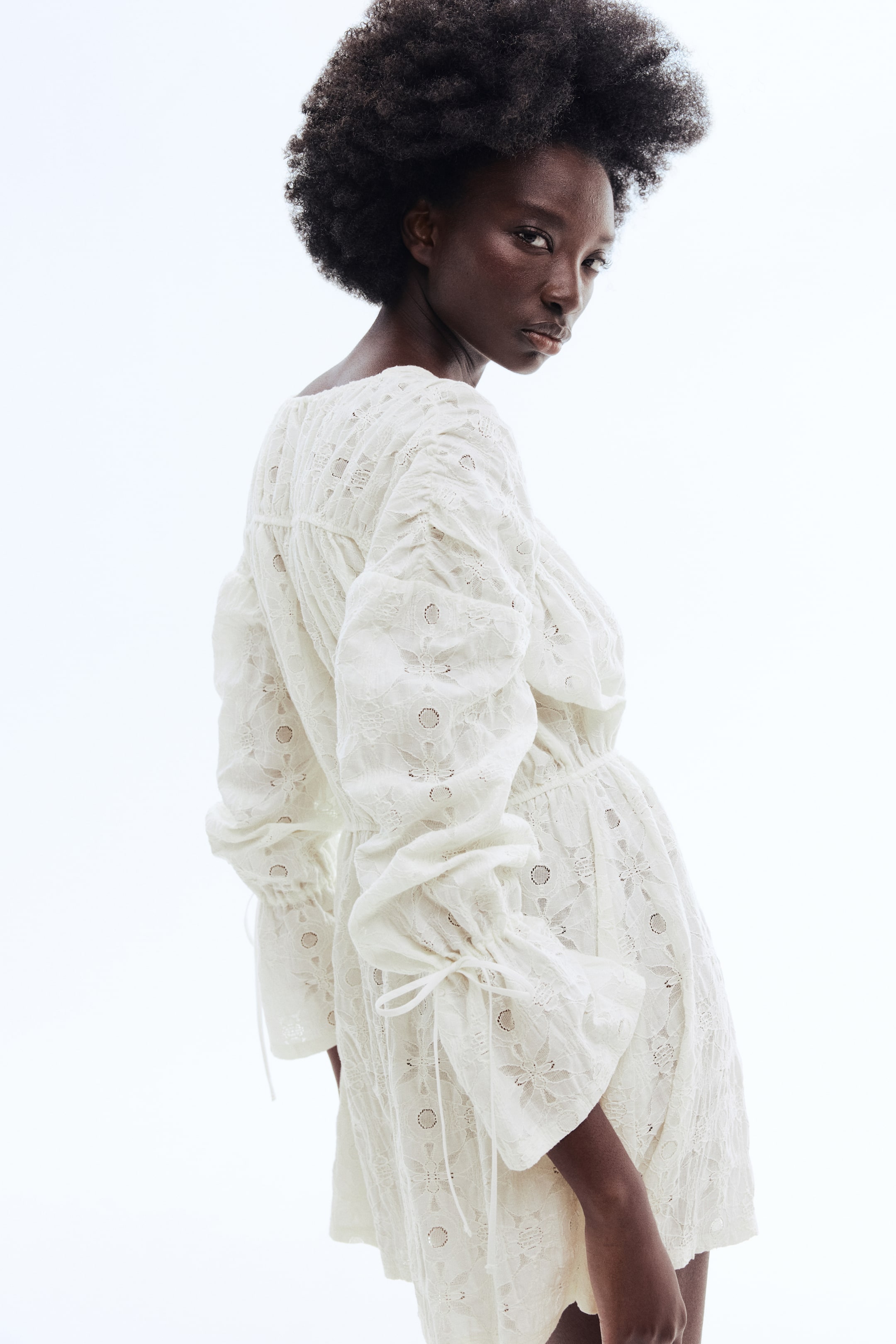 Visa större bild: En vit broderad jumpsuit med voluminösa långa ärmar och knytmanschetter samt en rynkad elastisk midja, visar upp ett blommigt broderimönster från en bakifrån-vinkel.