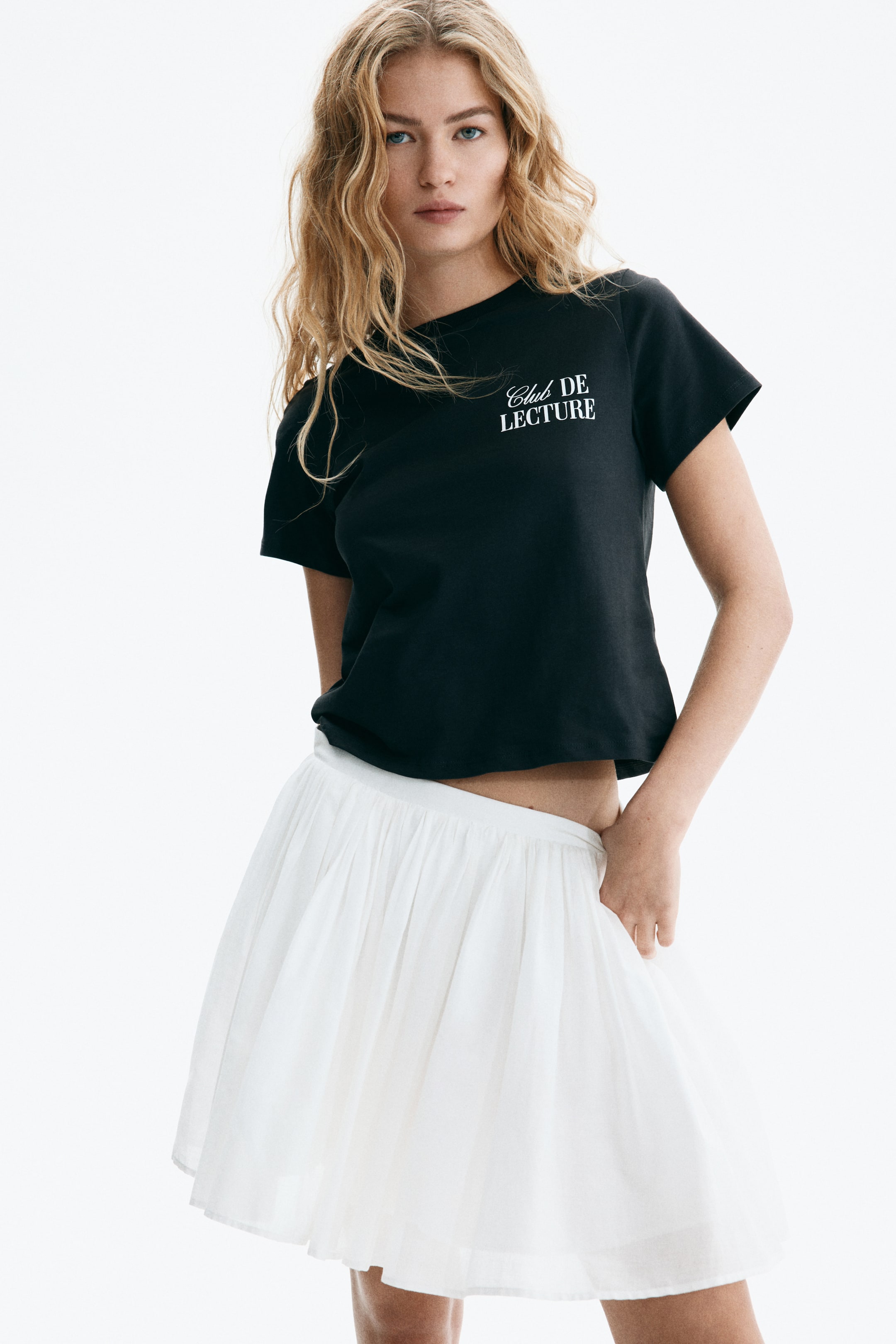 View larger image: A black T-shirt is angled slightly forward and to the right, displaying a crew neck, short sleeves and a cropped hem. White embroidered text reading 'Club DE LECTURE' appears on the left chest.