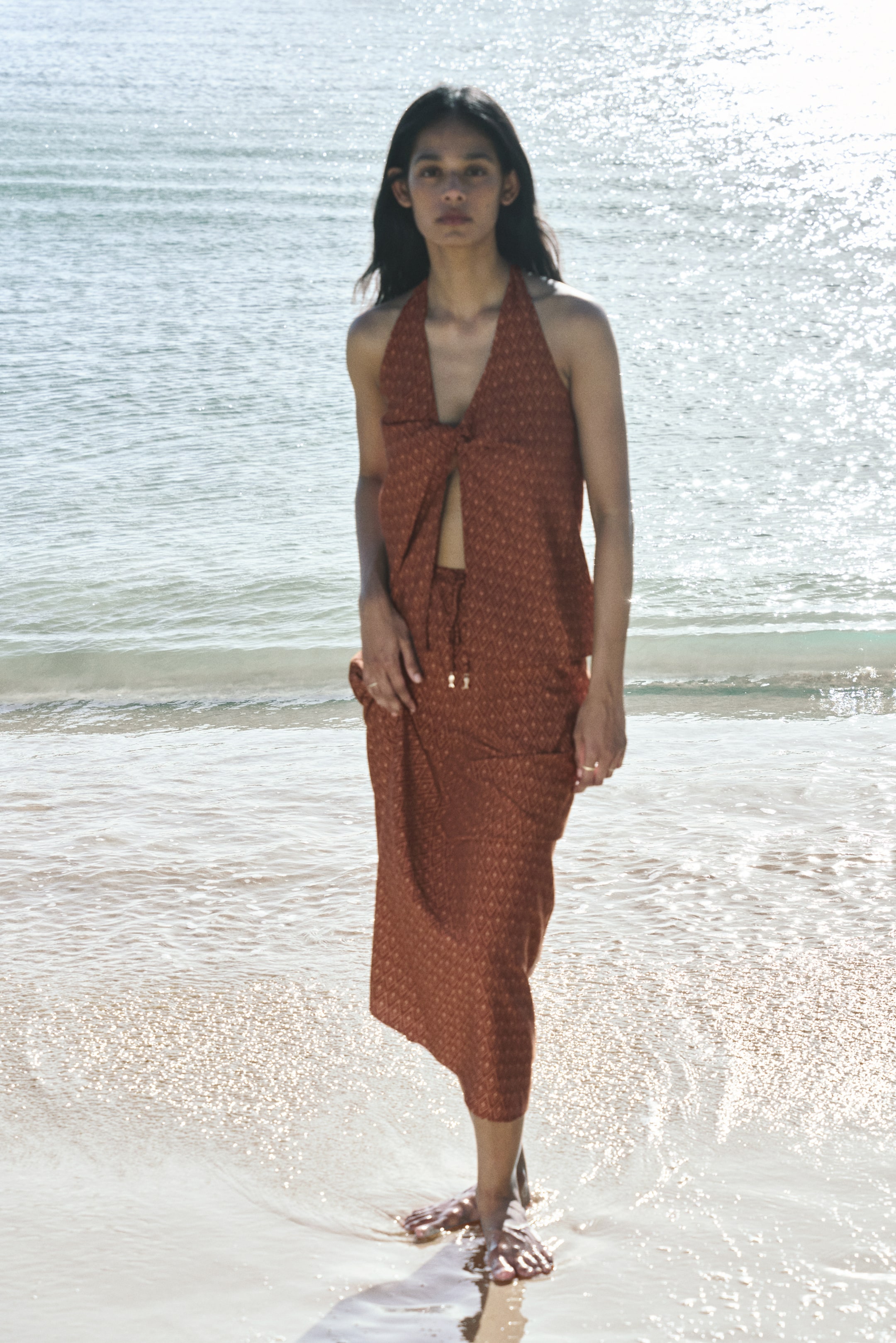 View larger image: The model is showcasing an ankle-length, loose-fit skirt with a regular waist and a narrow drawstring. This piece features a subtle geometric pattern, perfectly paired with a matching top. The model elegantly holds the skirt with one hand near the hip, highlighting its stylish design.
