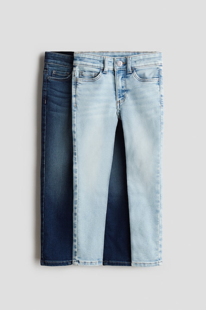 Twee paar 5-pocket denim jeans worden getoond met hun voorkant naar voren gericht: een lichtblauwe wassing ligt over een donkerblauwe wassing. De lichtblauwe jeans aan de voorkant hebben een knoopsluiting, ritssluiting, twee voorzakken en een muntzakje, terwijl beide paren een skinny fit door de heup, dij en been laten zien. - 1