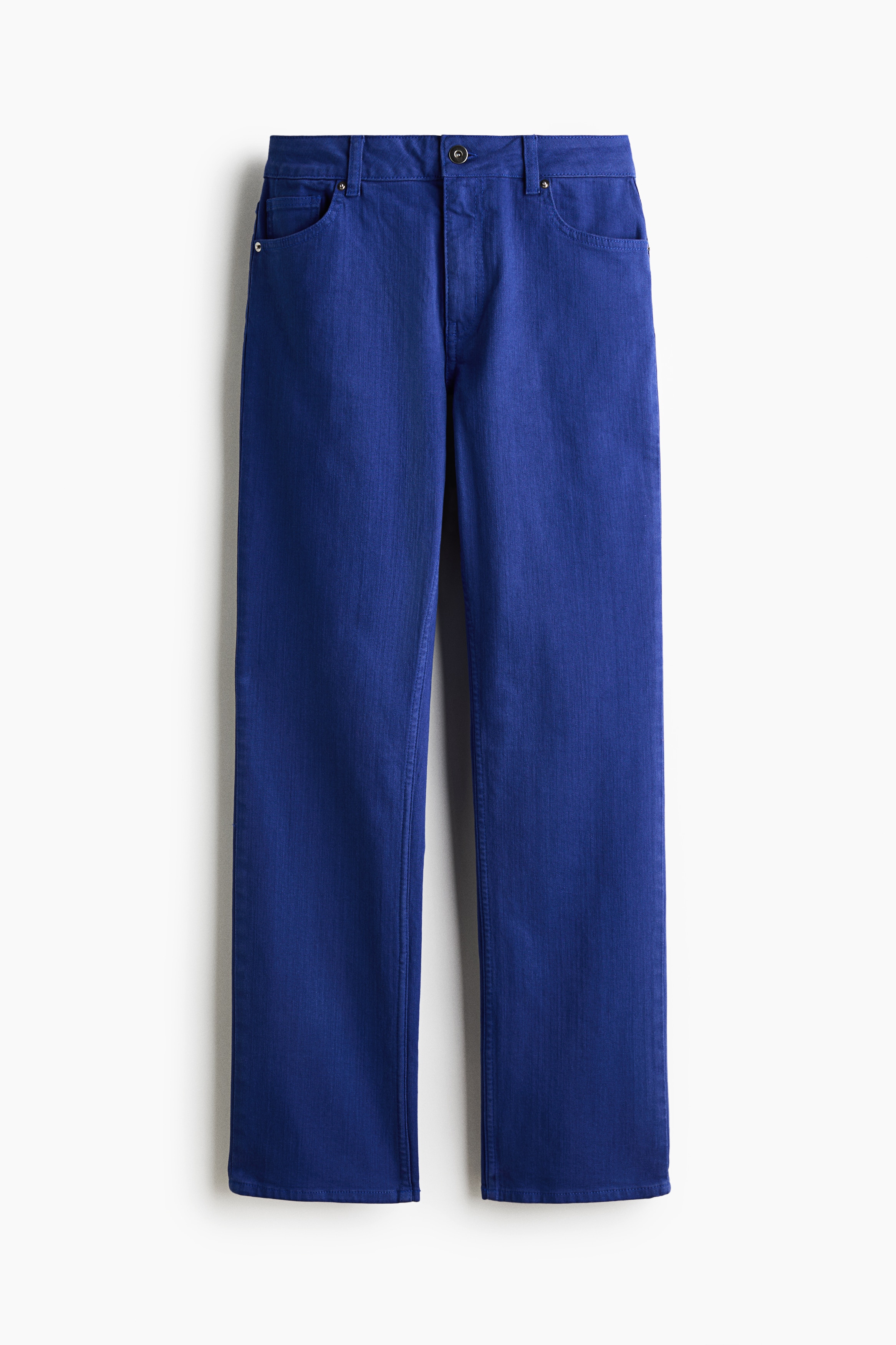 Pantaloni in twill viola a vita alta con gamba slim, indossati dalla modella in posa con una mano appoggiata nella tasca anteriore. I pantaloni sono abbinati a un crop top nero, una giacca di pelle nera e sandali neri con tacco.