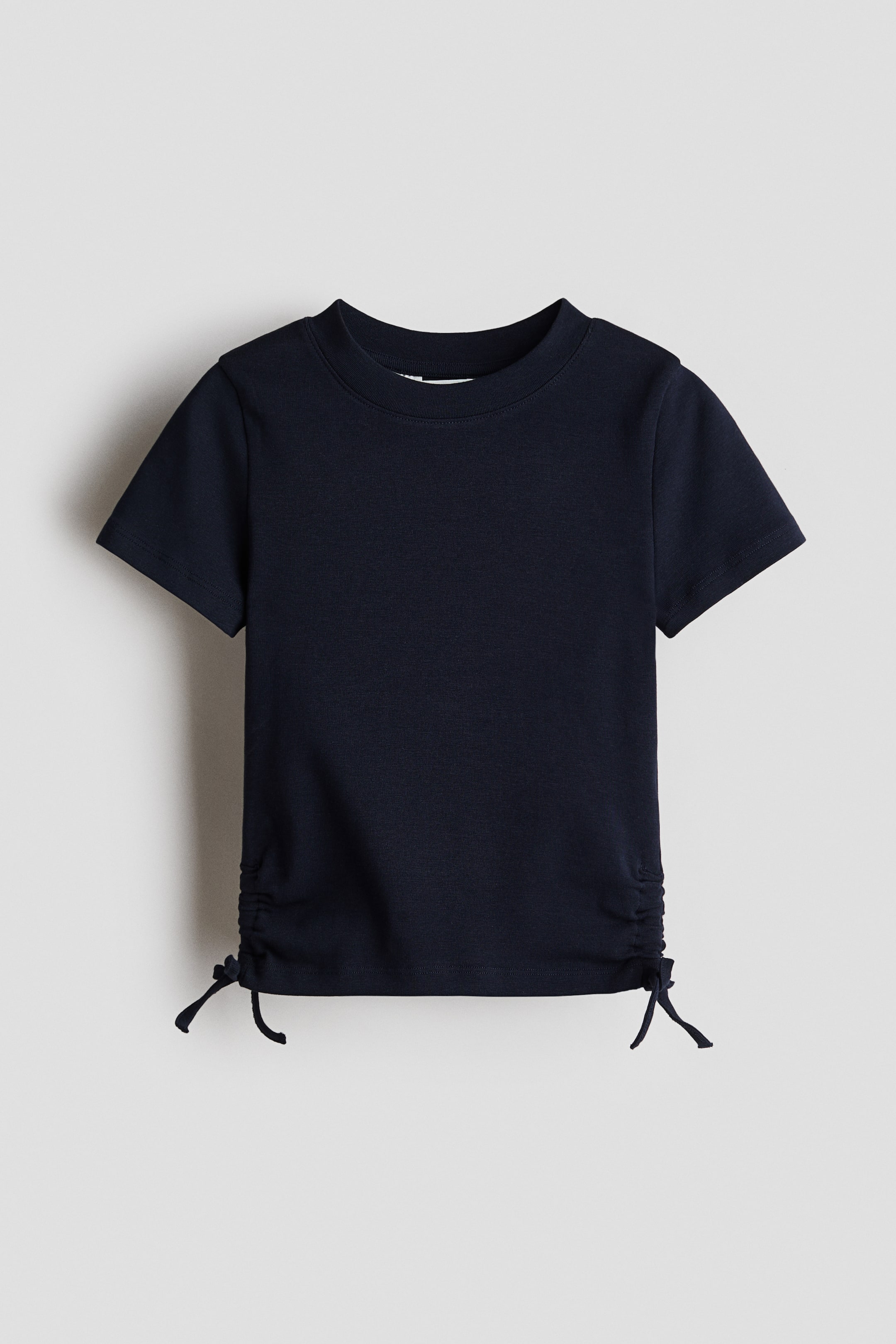 View larger image: A navy short-sleeved top in cotton jersey is displayed from the front. It features a round neckline and decorative drawstrings with sewn-in bows on each side of the hem, creating a ruched effect.
