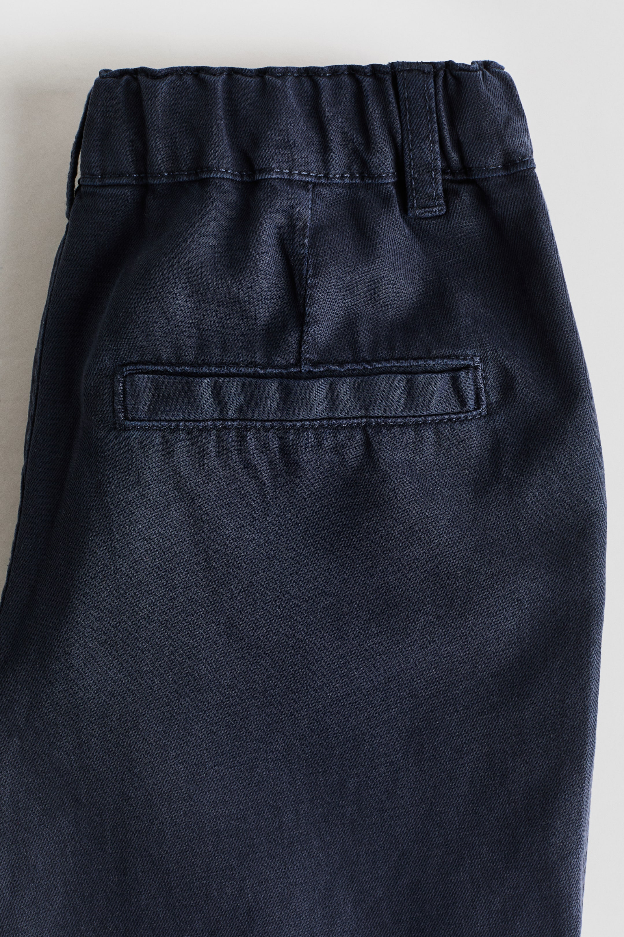 Ver imagen más grande: Los chinos de corte relajado en azul oscuro presentan una cintura elástica y fruncida en la parte posterior, con una única trabilla para cinturón y un bolsillo ribeteado horizontal falso situado debajo, todo en tejido de sarga.
