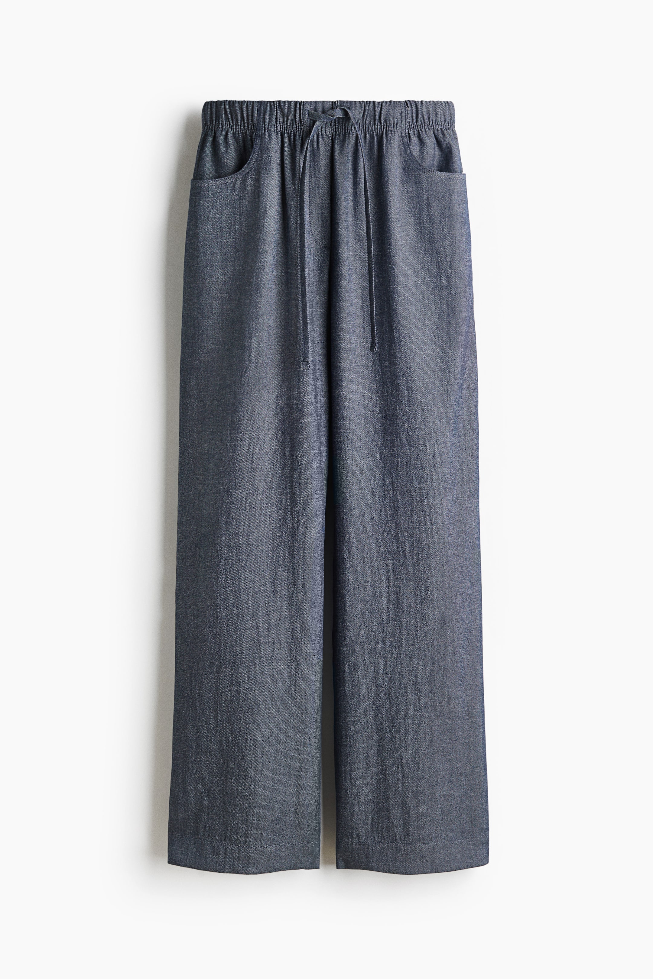 View larger image: The dark blue-grey trousers, showcasing a subtle woven texture, come with an elasticated waistband highlighted by a visible drawstring tie and two angled side pockets. They feature a straight, relaxed leg cut.