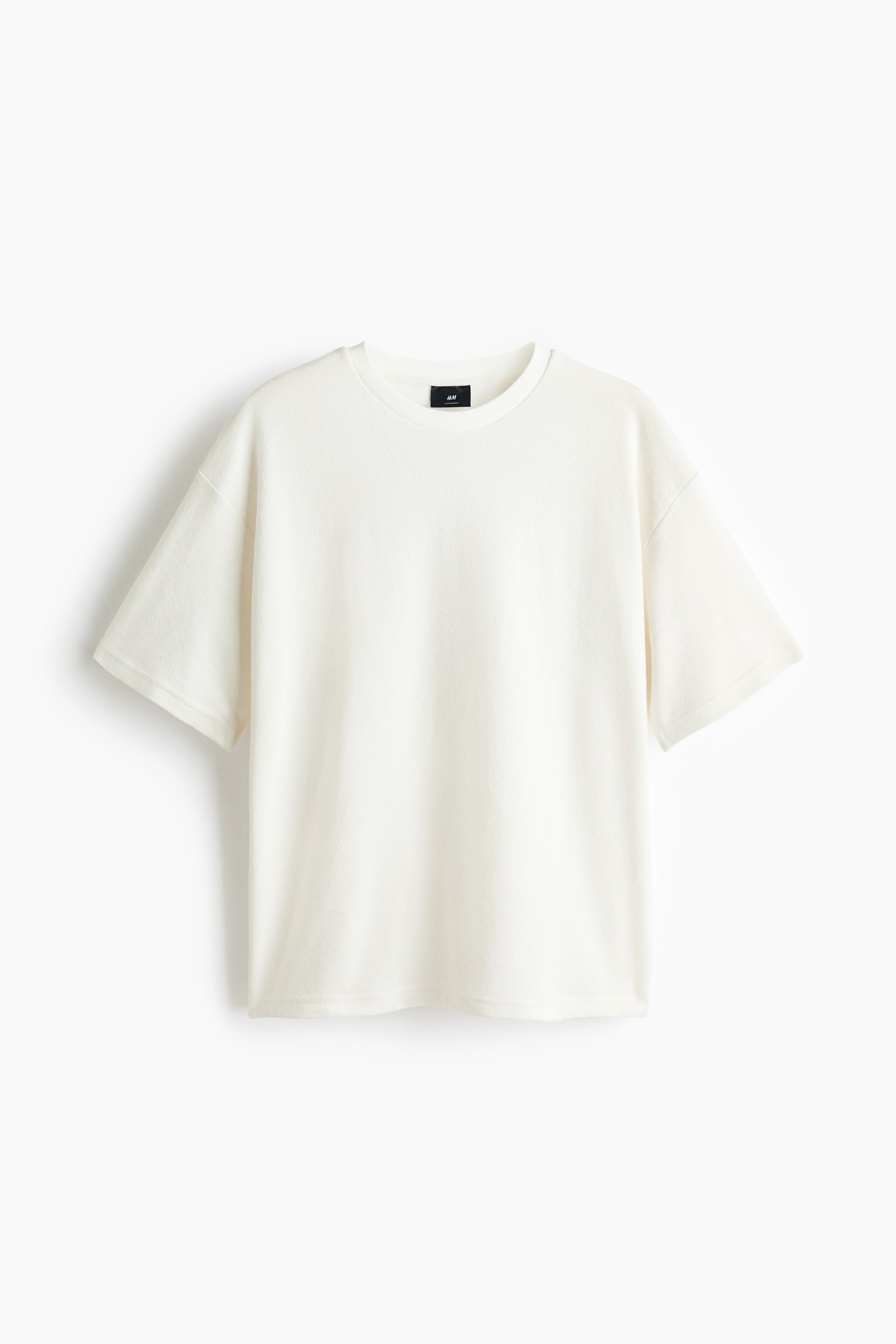 Προβολή μεγαλύτερης εικόνας: Το off-white T-shirt παρουσιάζει άνετη εφαρμογή από μπροστά, με στρογγυλή λαιμόκοψη και κοντά μανίκια με χαμηλωμένους ώμους. Στο εσωτερικό πίσω μέρος του γιακά διακρίνεται μαύρη ετικέτα της μάρκας.