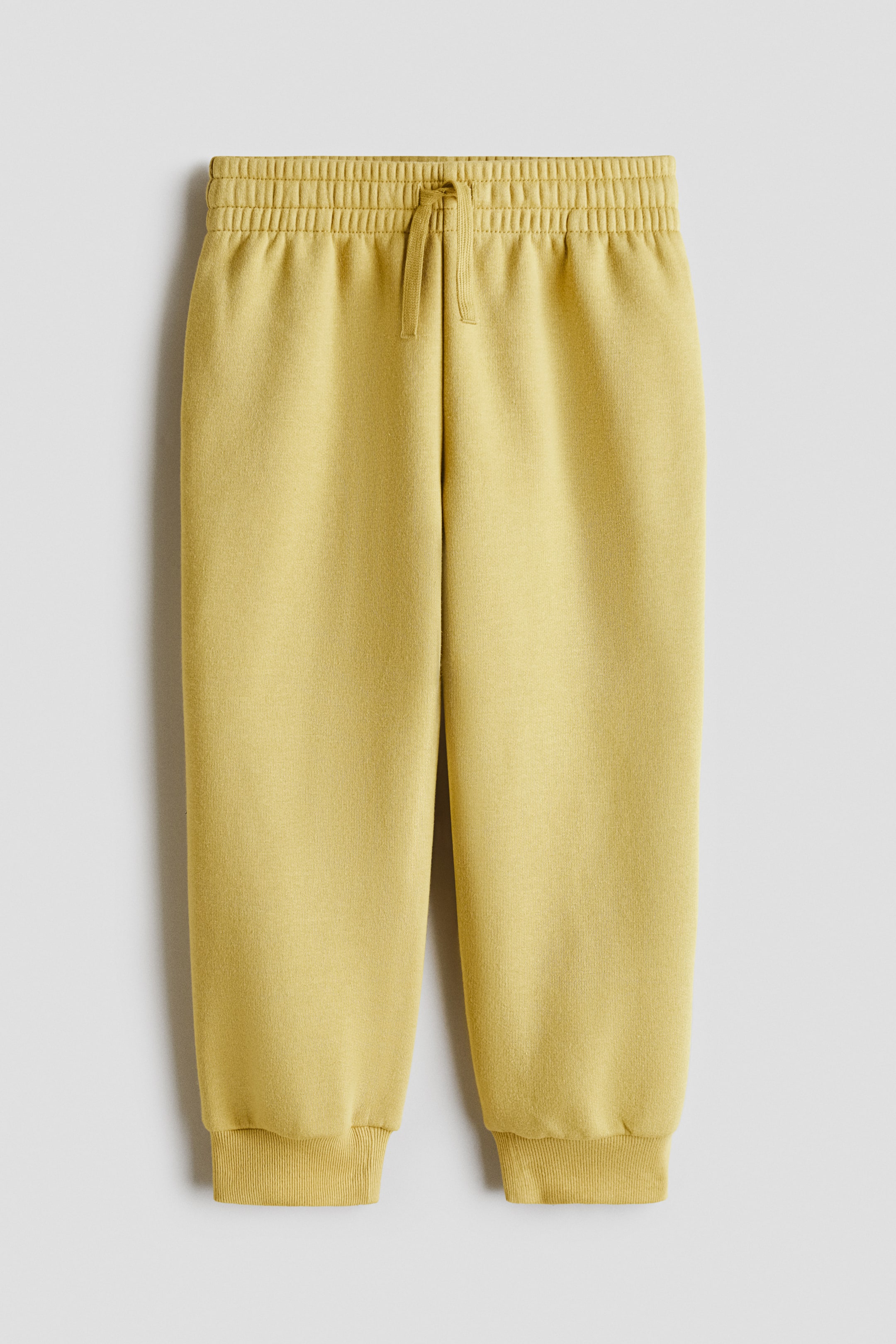 Ampliar la imagen: Un par de joggers color amarillo chartreuse muestra una vista frontal, confeccionados en una suave tela de sudadera. Presentan cintura elástica con cordón ajustable y bastillas con ribete acanalado.
