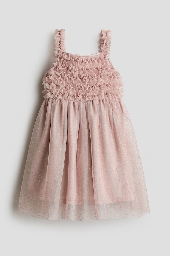 Une robe pour enfant rose pÃ¢le est prÃ©sentÃ©e de face, mettant en valeur un corsage recouvert de rangÃ©es horizontales denses de volants et de bretelles Ã  volants assorties. La robe se dÃ©ploie en une jupe trapÃ¨ze qui prÃ©sente une sous-couche rose unie sous un tulle vaporeux parsemÃ© de paillettes. - 1