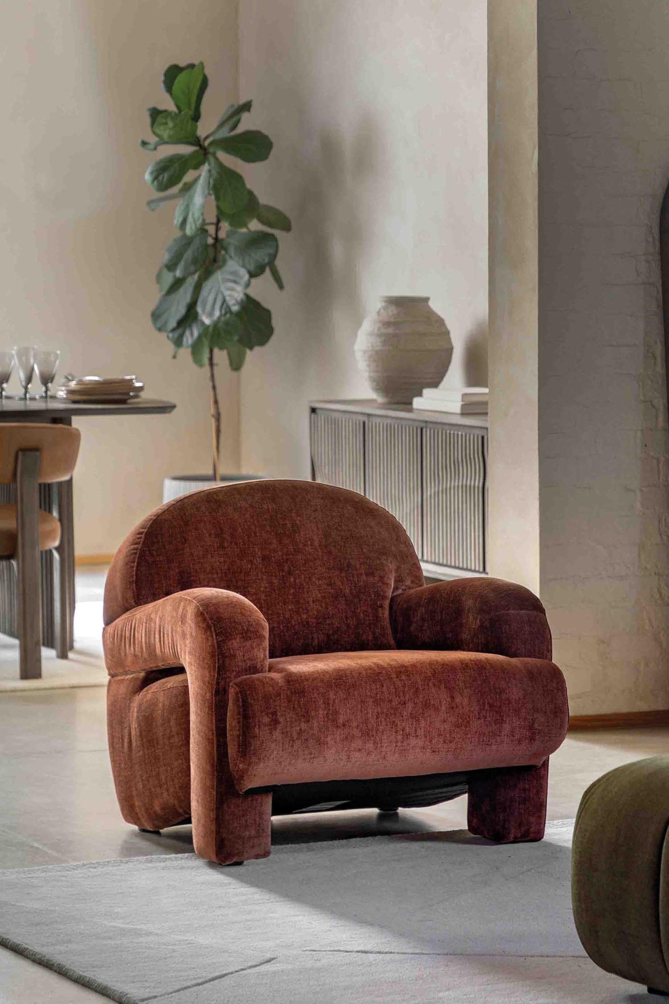 View larger image: A rust-coloured armchair is showcasing its rounded, bulky design, angled slightly to the right. It is upholstered in a textured fabric, featuring thick, curved armrests and a low, integrated block-like base.
