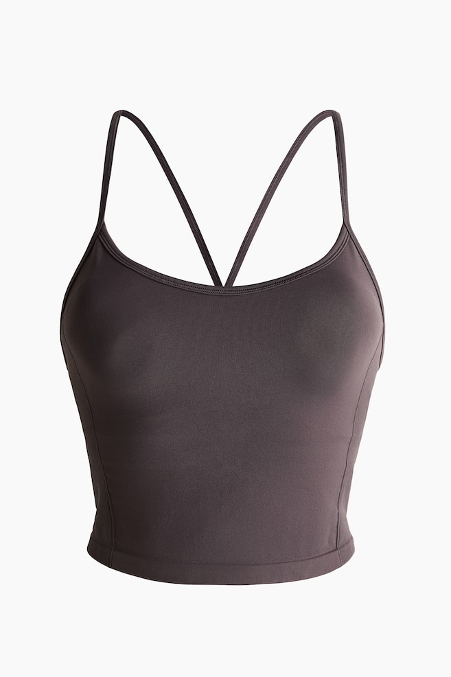 A seamless sports top in dark grey is shown from the front, featuring a scoop neckline, thin spaghetti straps crossing at the back, and a cropped, fitted silhouette. - 1