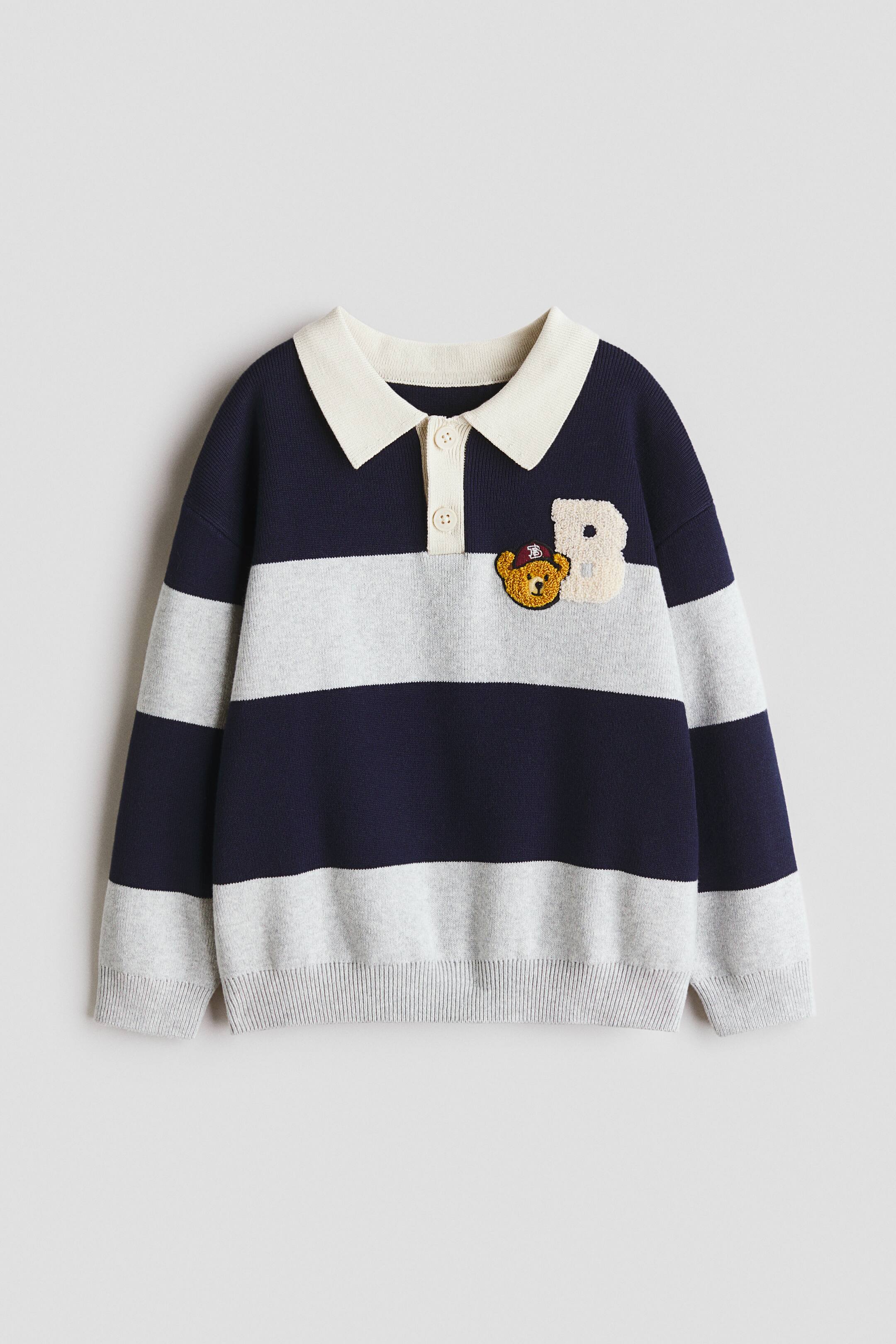 View larger image: A long-sleeved jumper is facing forward, showcasing broad navy blue and light grey horizontal stripes. It features an off-white collar with a two-button placket, and ribbed cuffs and hem. On the left chest, a teddy bear appliqué appears next to a textured cream-coloured letter 'B'.