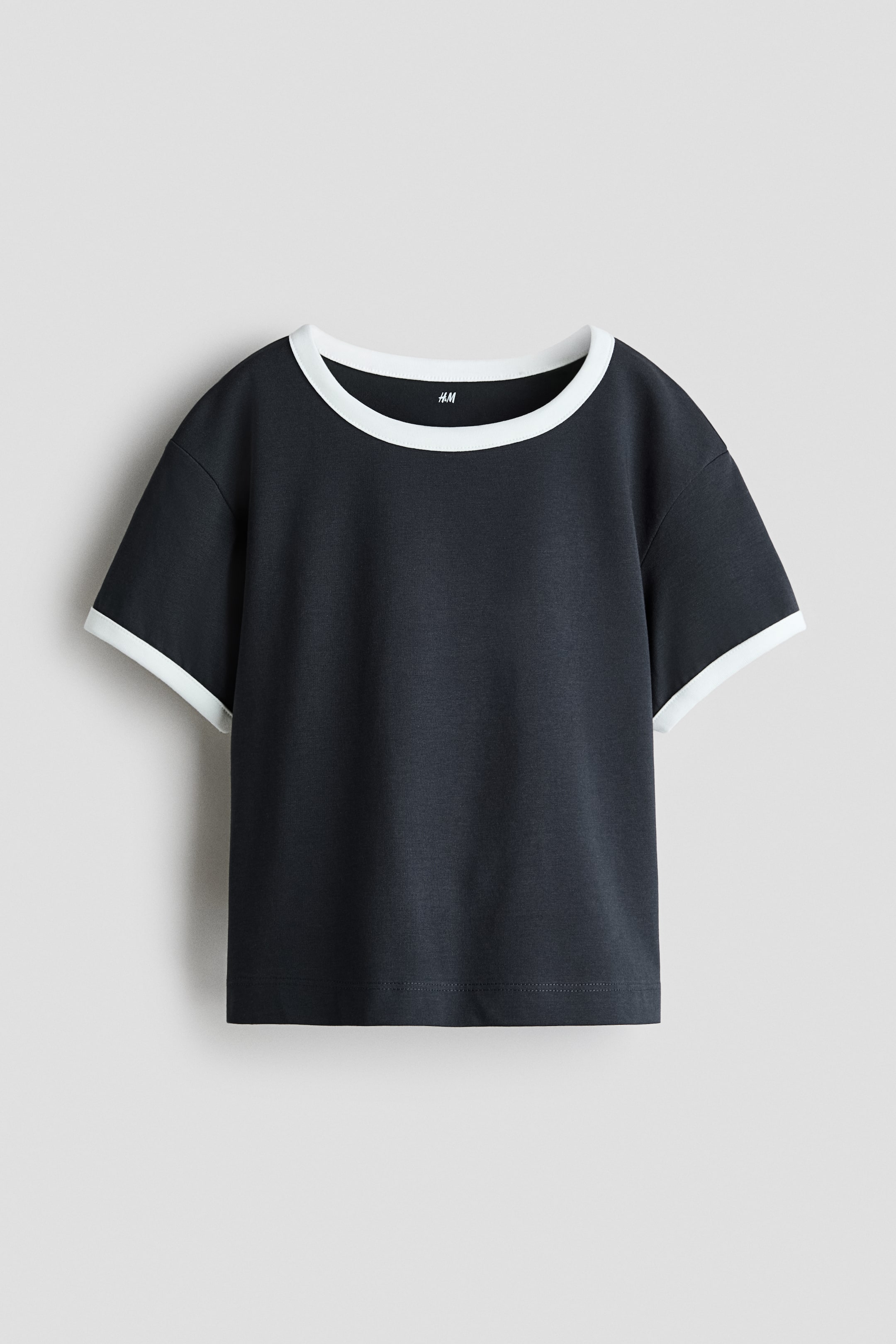 View larger image: A dark grey ringer t-shirt is shown from the front, featuring a contrasting white crew neck and matching white trim on the short sleeves. The shirt has a relaxed, boxy fit with a straight hem.