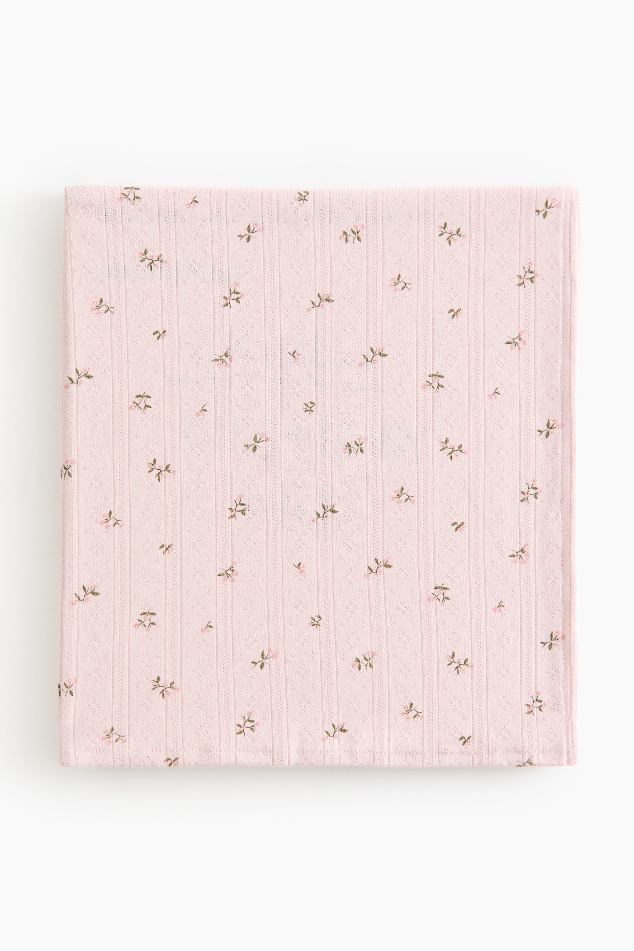View larger image: The baby blanket is neatly folded, showcasing its front in a soft pink pointelle-knit cotton fabric, adorned with a timeless floral pattern of delicate pink flowers and green leaves.