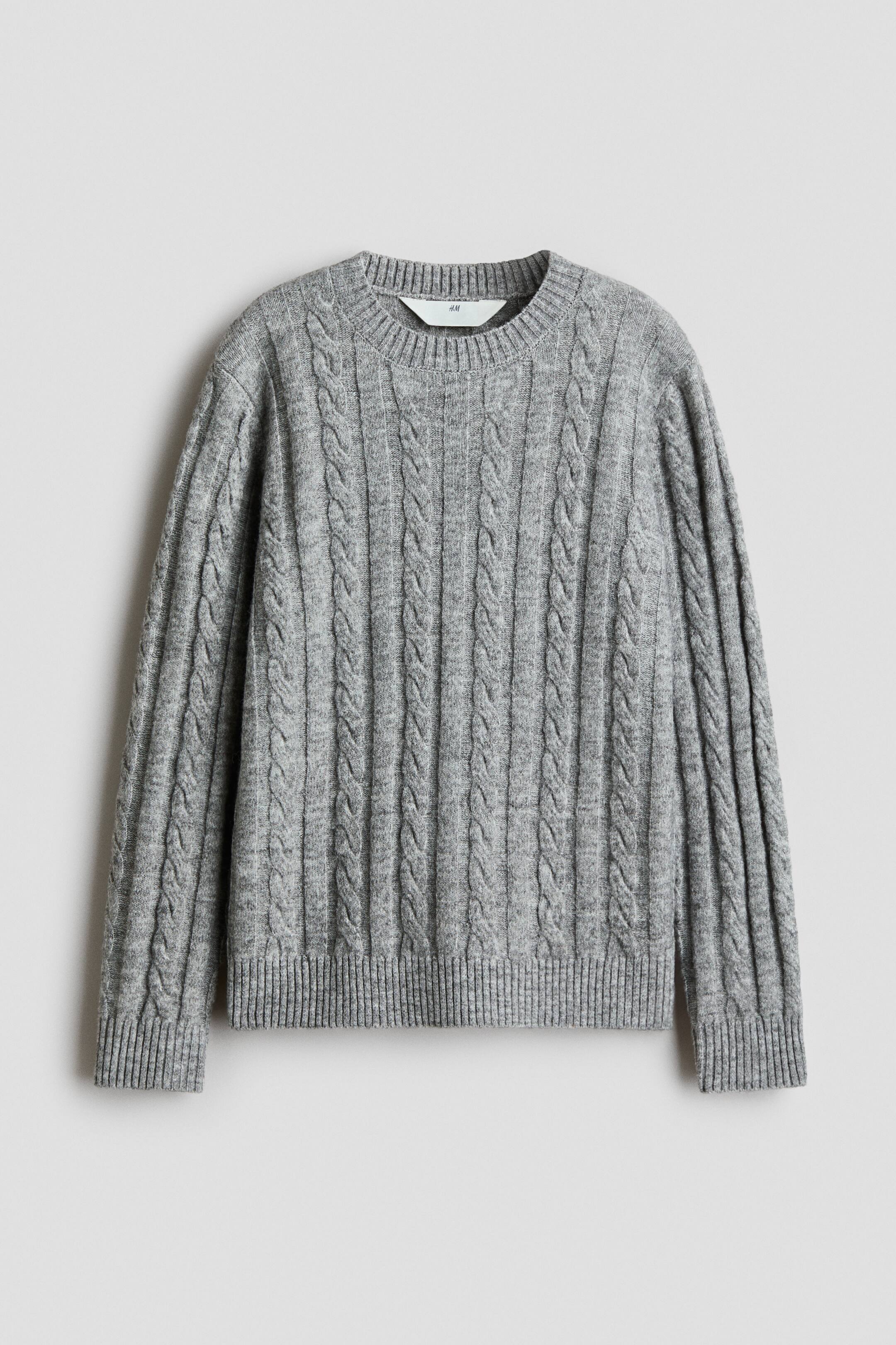 Agrandir l'image: Un pull gris à torsades est présenté de face, avec un motif vertical de torsades tressées sur l’ensemble du corps et des manches longues. Il est conçu avec un col rond côtelé, des poignets côtelés et un ourlet côtelé assorti.