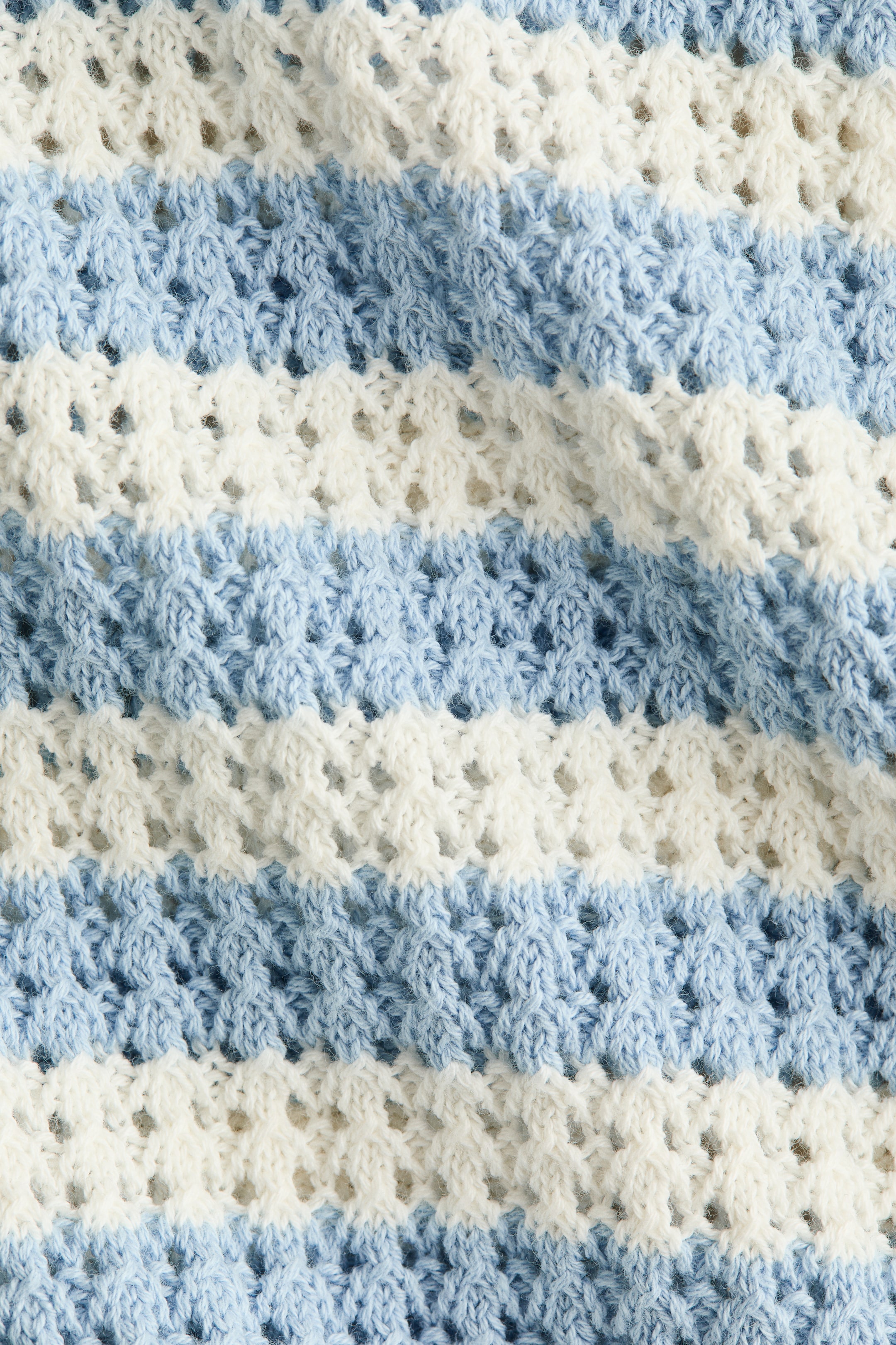 Größeres Bild ansehen: Der Pulloverstoff zeigt horizontale Streifen in abwechselnd hellblau und weiß, mit einer weichen, pointellen Stricktextur und kleinen offenen Details.