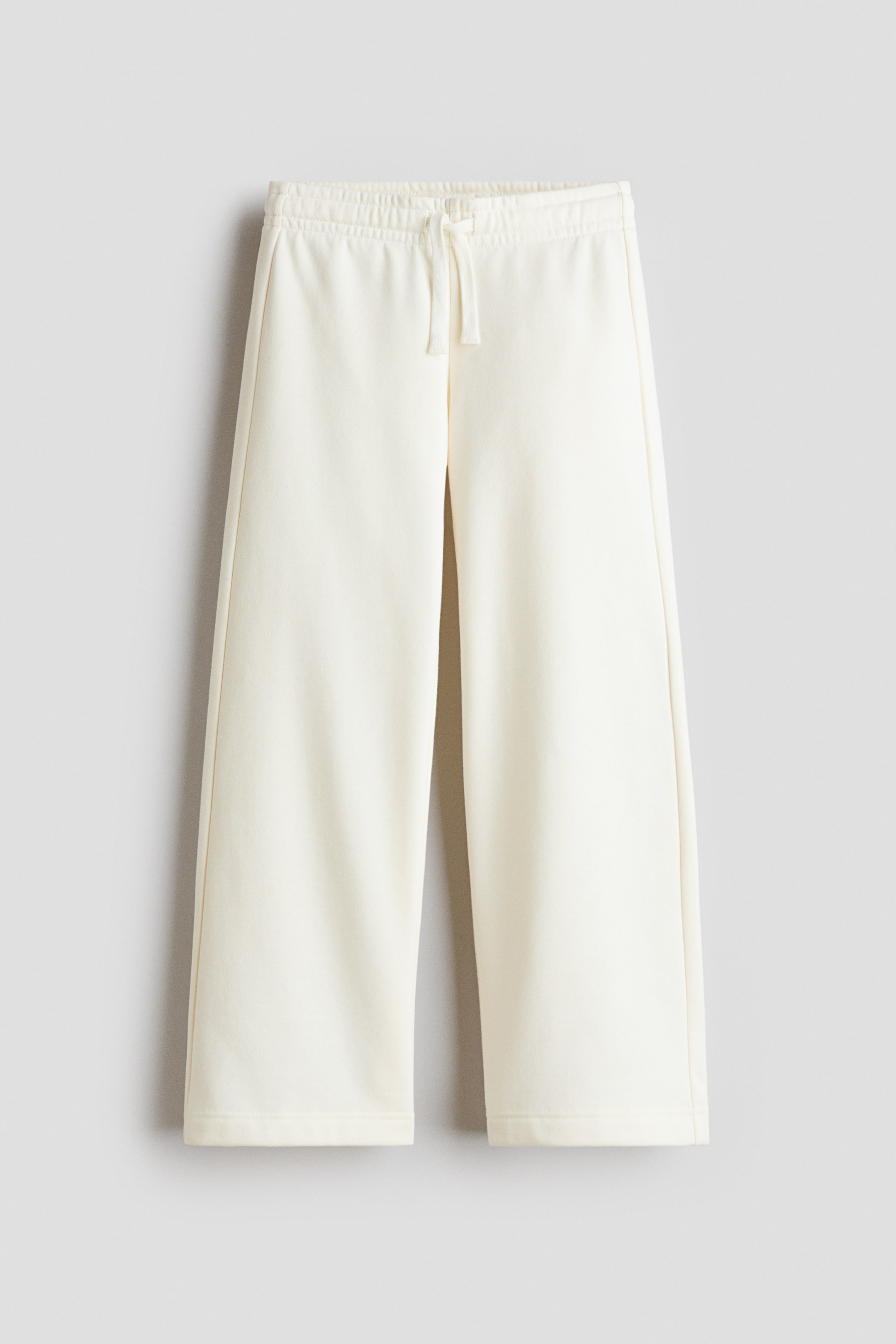 Visualizza l'immagine ingrandita: Una vista frontale di pantaloni sportivi a gamba larga color crema mostra una vita elasticizzata con coulisse regolabile coordinata. I pantaloni sono appesi dritti, mettendo in evidenza una silhouette rilassata a gamba larga con orli cuciti puliti.