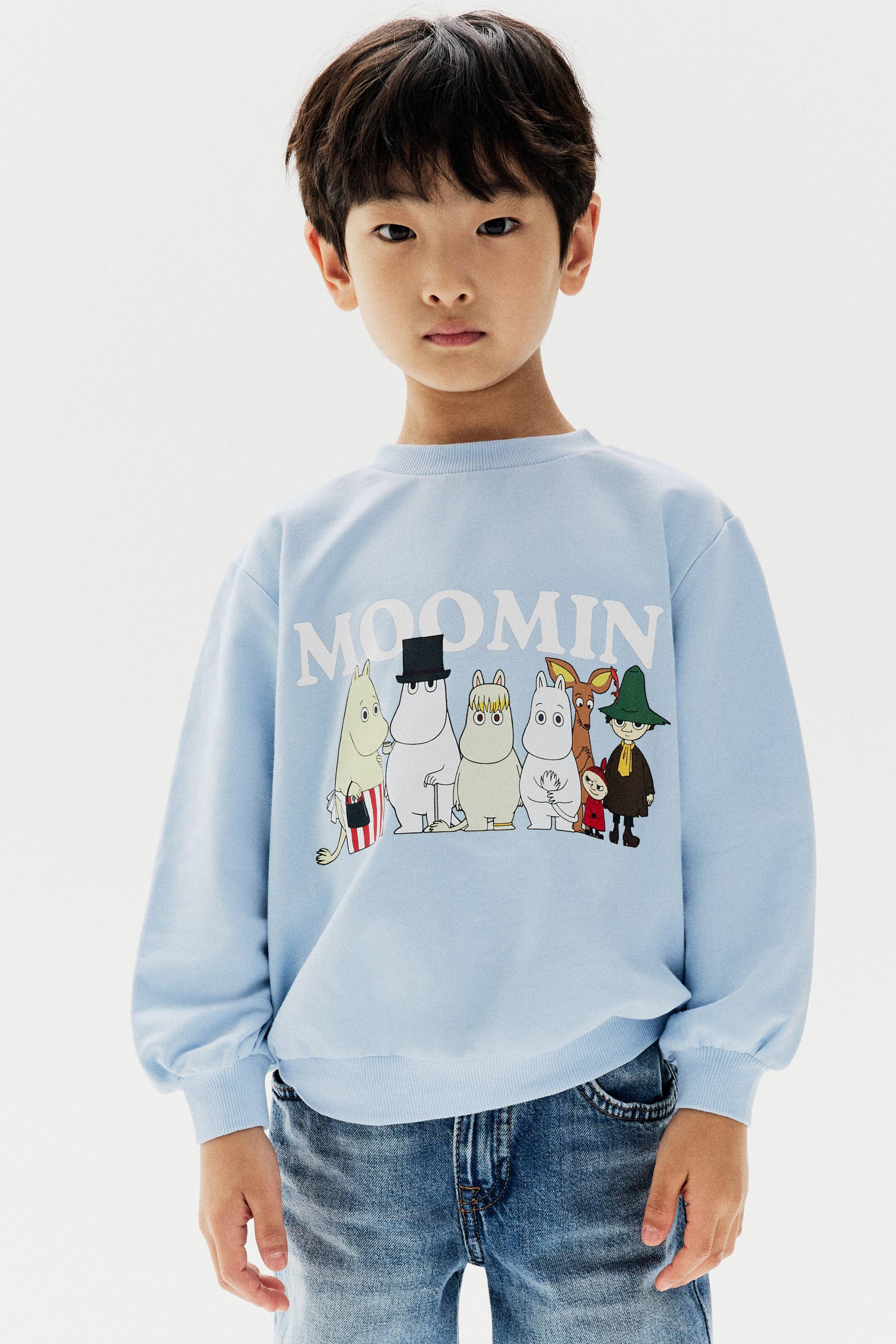 查看大圖: 模特兒穿著一件淺藍色運動衫,正面飾有Moomin角色圖案印花。這款上衣採圓領羅紋領口、落肩設計,以及羅紋袖口與下擺,並搭配藍色牛仔褲。