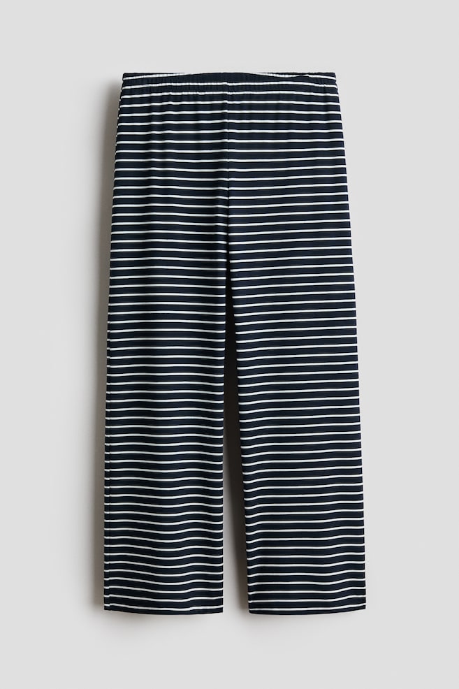 A pair of wide-leg jersey joggers featuring a navy and white horizontal stripe pattern is hanging facing the front. The trousers are showcasing a gathered elasticated waistband and a straight, wide-cut leg design. - 1