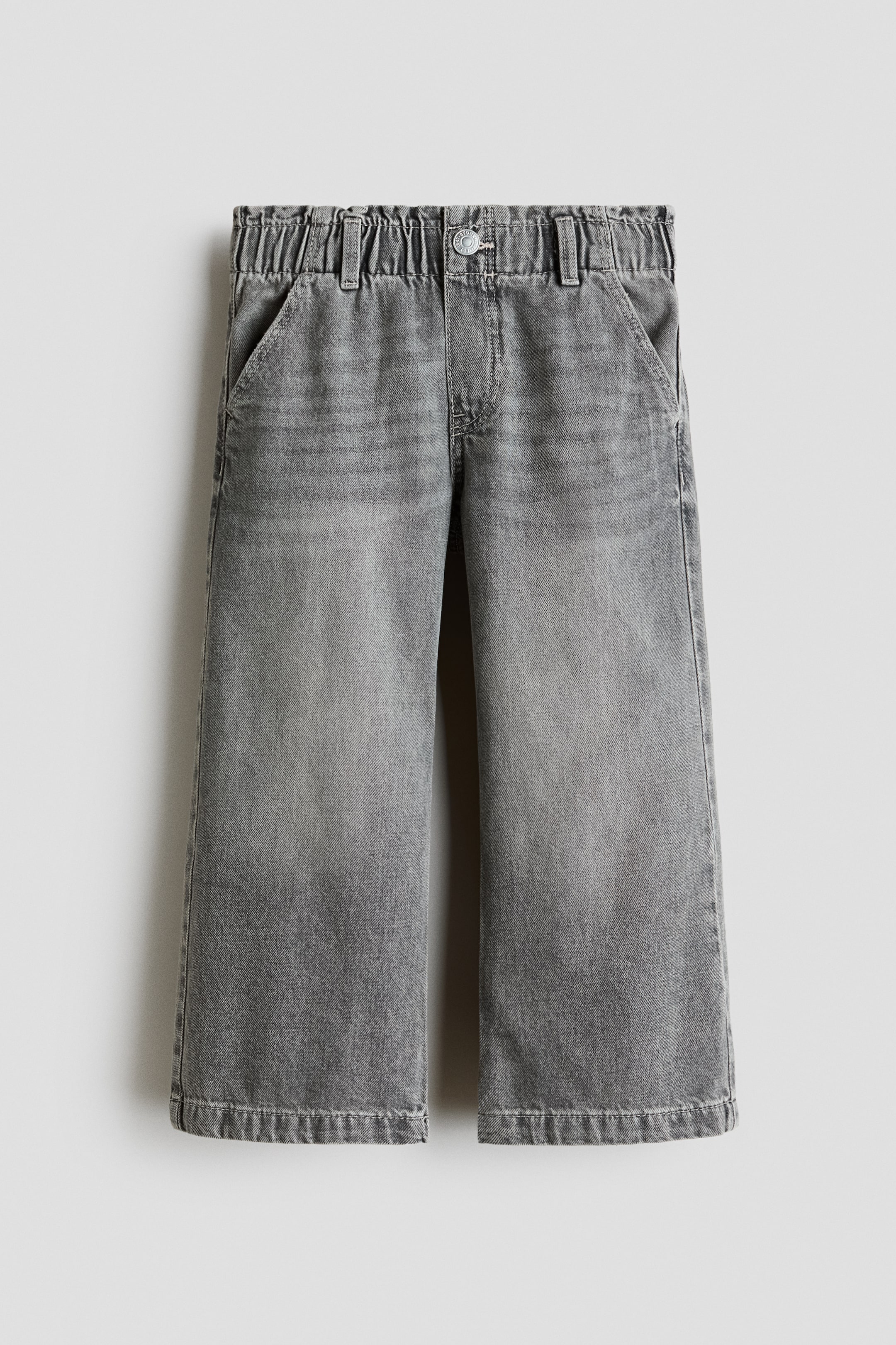 View larger image: Grey cotton denim jeans are showcased from the front, highlighting wide legs, an elasticized paper bag waist, a faux fly with a button, and diagonal side pockets.