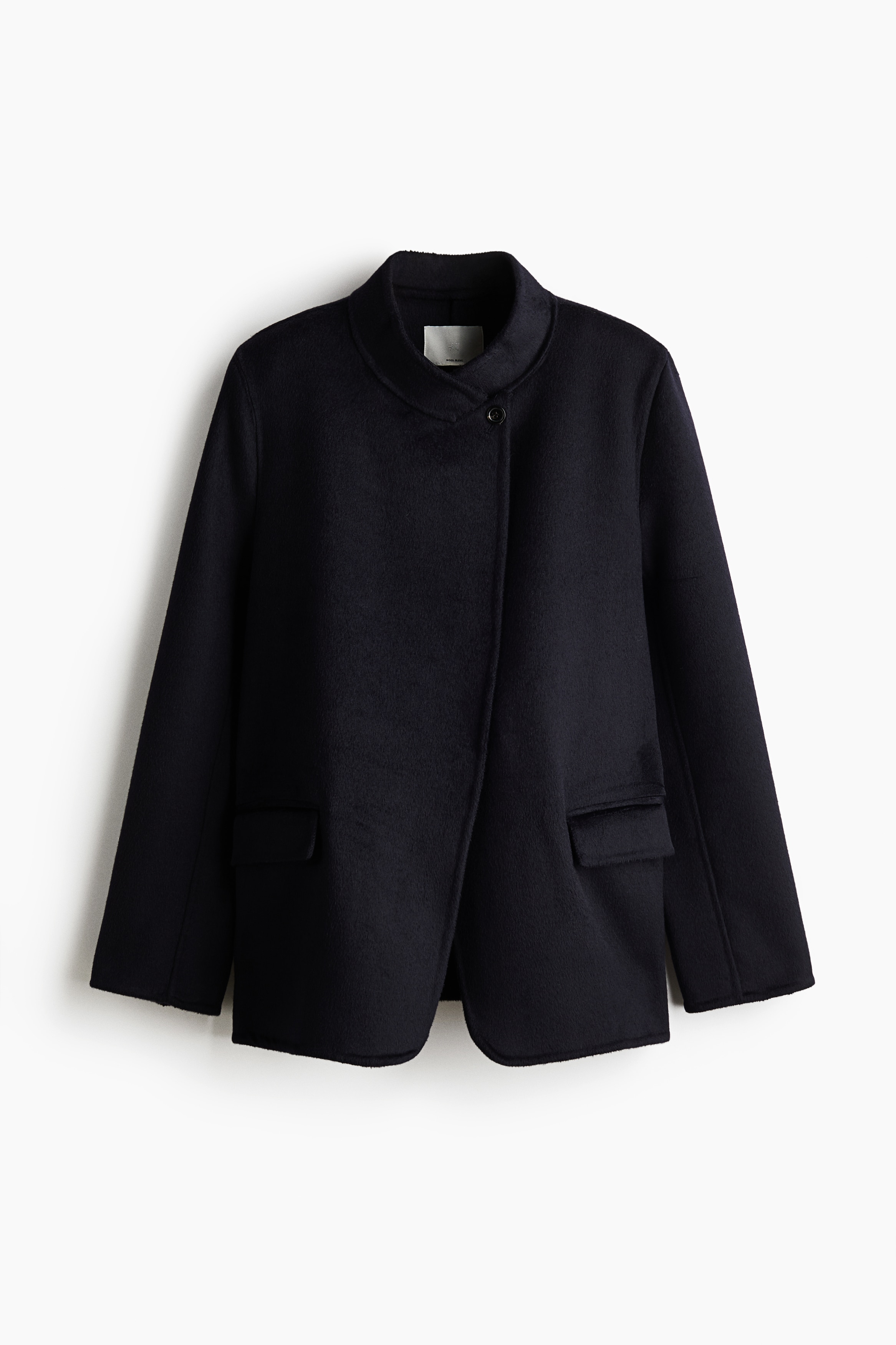 Keten gÃ¶rÃ¼nÃ¼mlÃ¼ yÃ¼n karÄ±ÅÄ±mÄ±ndan siyah, tek sÄ±ra dÃ¼Ämeli bir blazer, kollarÄ± Ã§aprazlanmÄ±Å Åekilde model tarafÄ±ndan giyiliyor. Blazer, dik yakaya ve tek gÃ¶rÃ¼nen dÃ¼Ämeli, hafif kaydÄ±rÄ±lmÄ±Å Ã¶n aÃ§Ä±klÄ±Äa sahip olup mavi ve siyah saten bir fularÄ±n Ã¼zerine katmanlanmÄ±ÅtÄ±r.