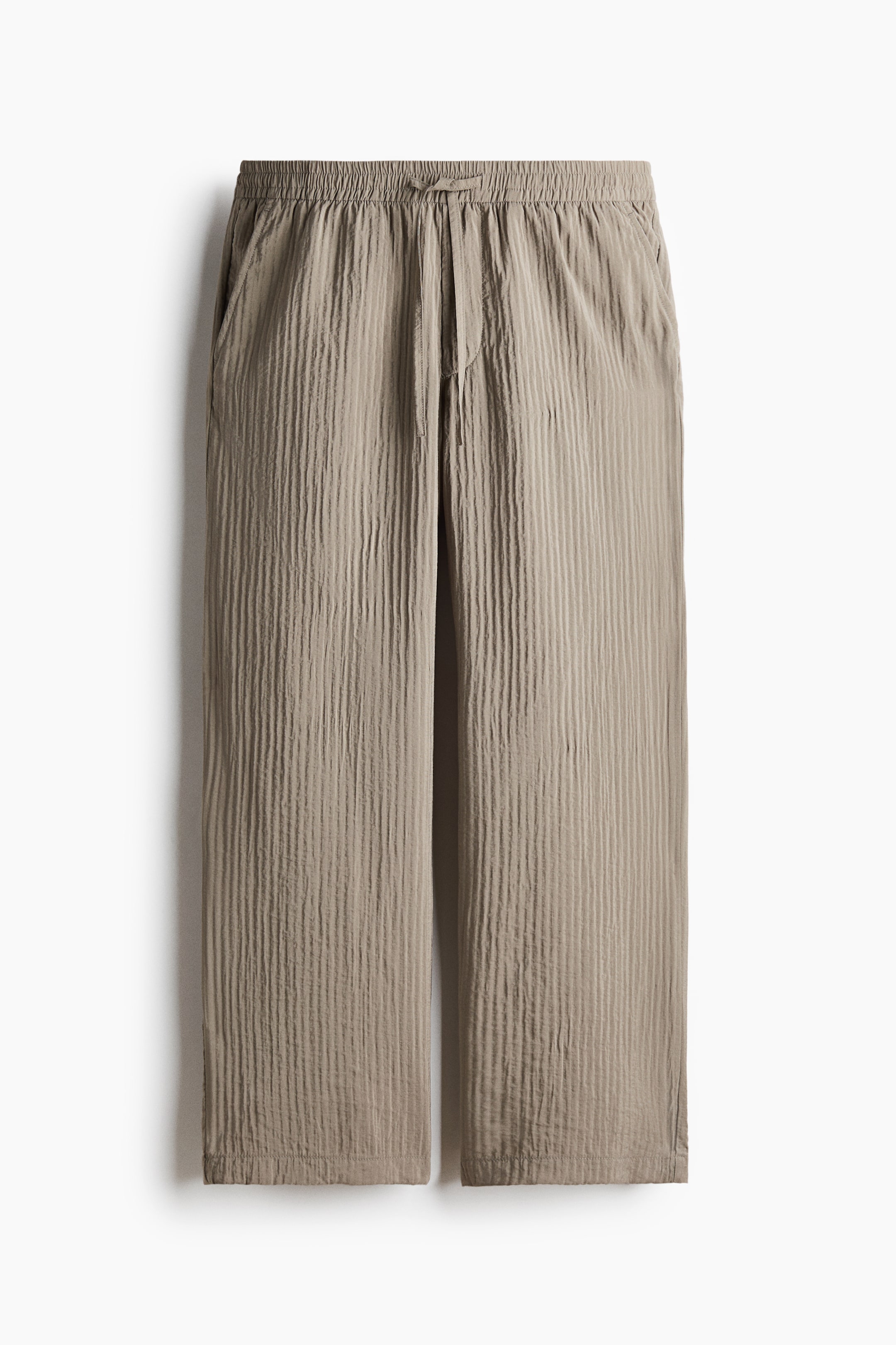 View larger image: The light brown trousers are shown in a front view, featuring an elasticated drawstring waistband and side pockets. They are designed in a crinkled, vertically textured fabric with a relaxed straight-leg fit.