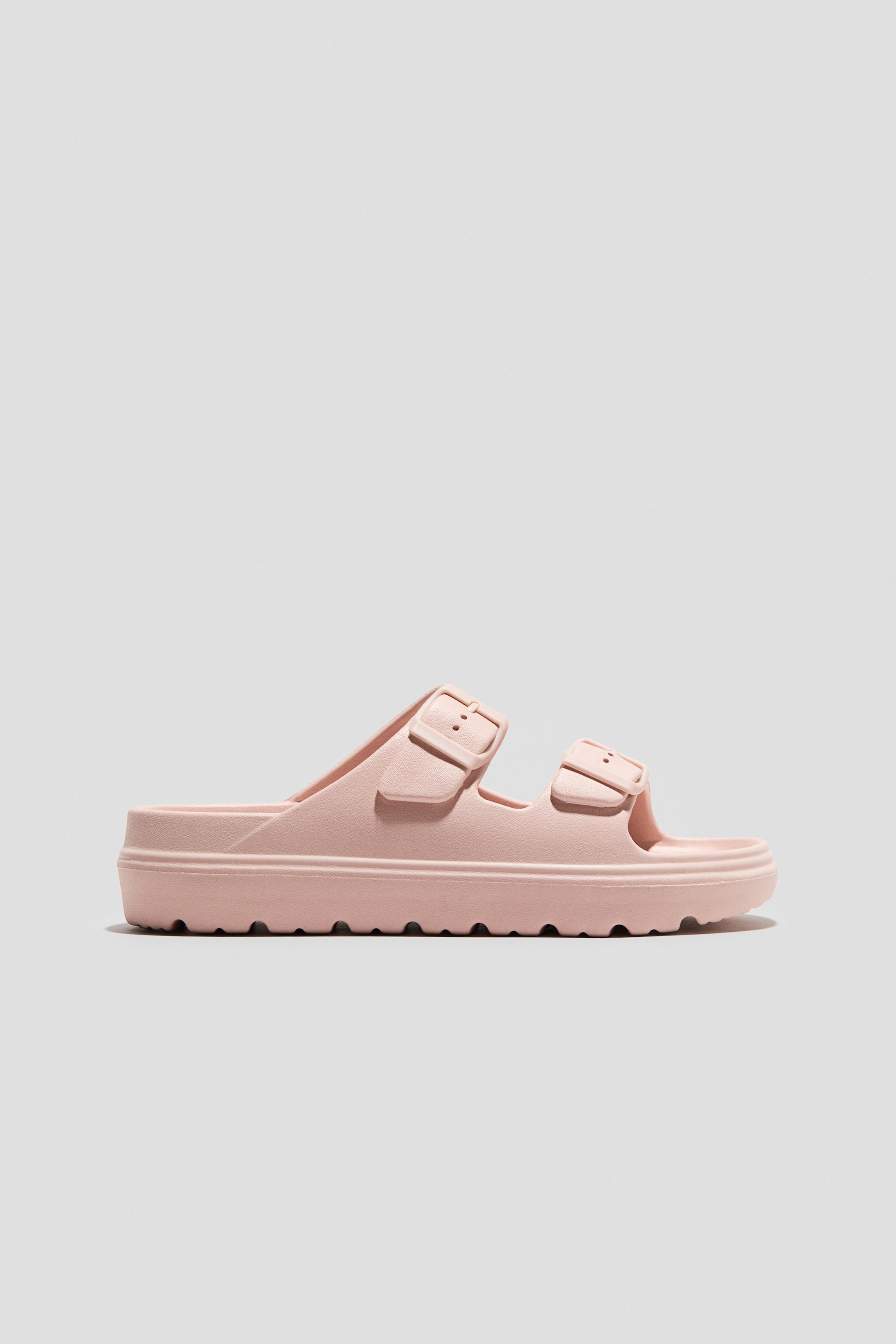 View larger image: A light pink slide sandal featuring two wide top straps with decorative, matching buckles and a thick platform sole with a rugged, textured tread pattern.