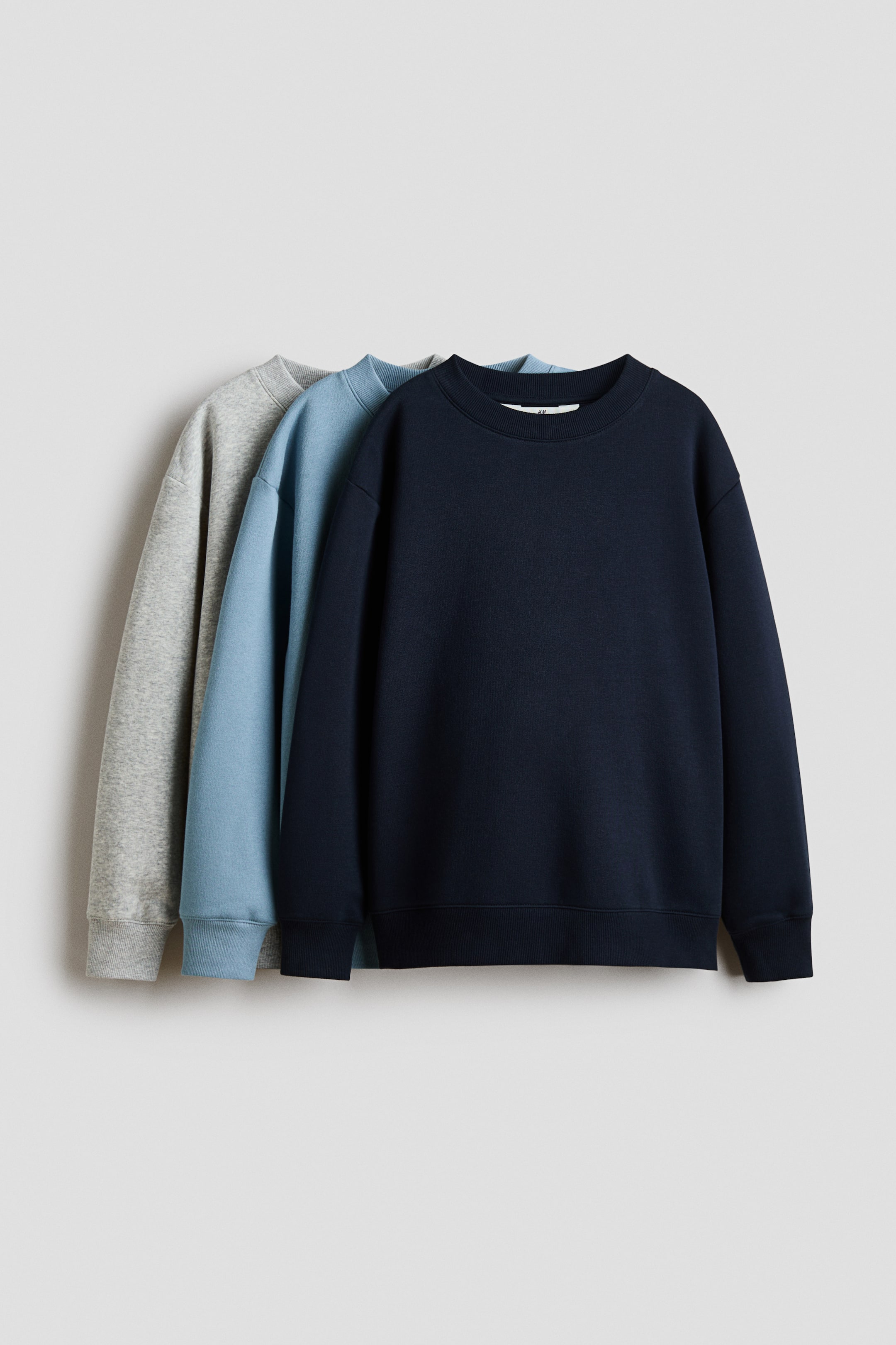 View larger image: Three fleece sweatshirts are shown from the front, layered in navy, light blue, and grey. Each sweatshirt features a round, rib-trimmed neckline, gently dropped shoulders, and ribbed cuffs and hem.