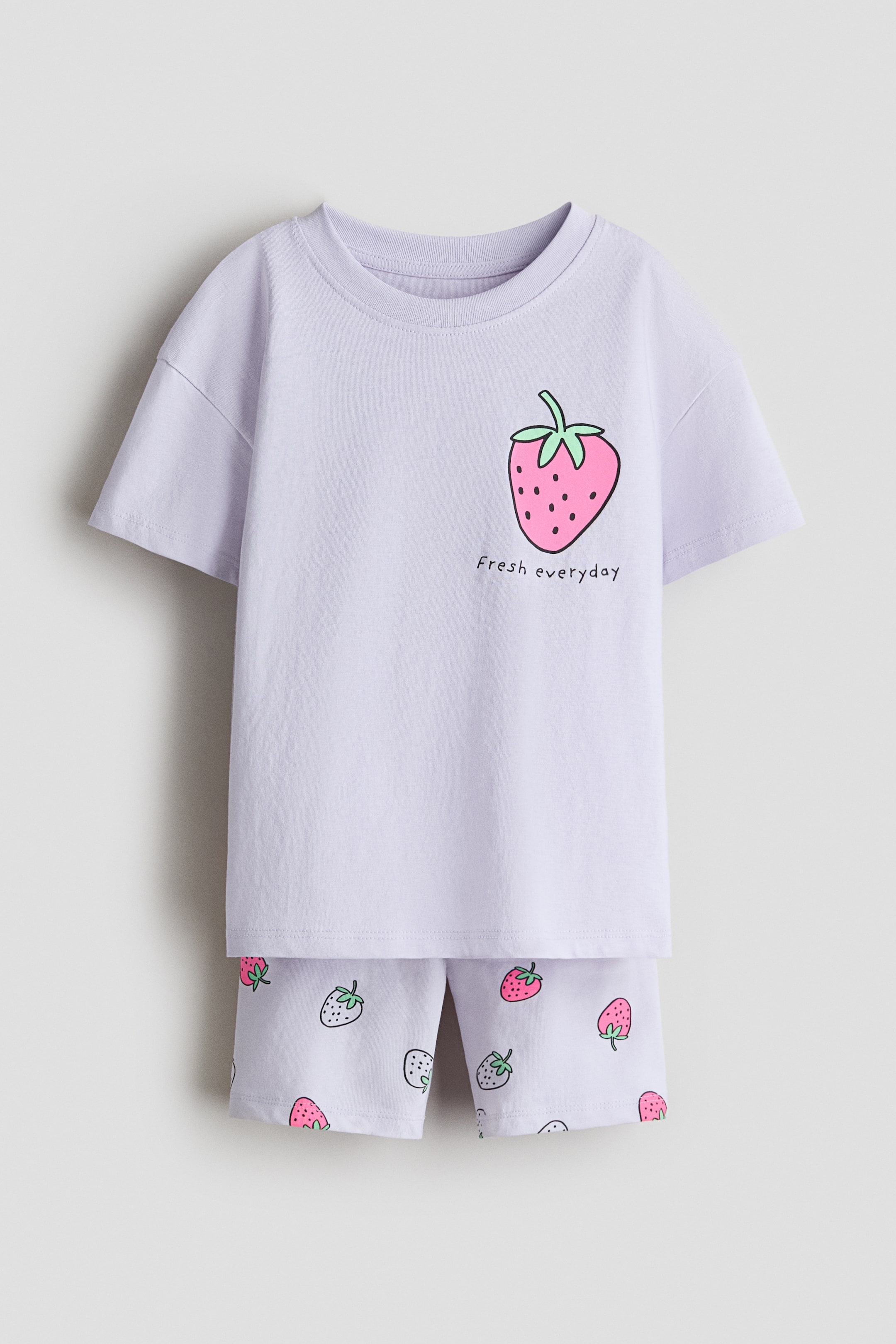 Größeres Bild anzeigen: Ein hellviolettes Set aus weichem, bedrucktem Baumwolljersey präsentiert ein T-Shirt mit geripptem Halsausschnitt, überschnittenen Schultern und einem großen rosa Erdbeer-Print mit dem Text "Fresh everyday" auf der Vorderseite. Die dazu passenden Radlerhosen zeigen einen Allover-Print mit kleineren Erdbeeren und verfügen über einen überzogenen elastischen Bund.