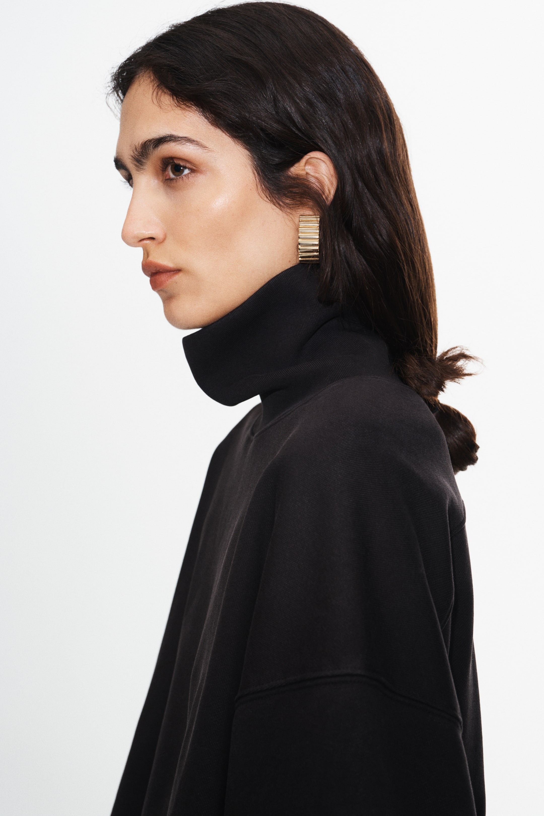 View larger image: A black, heavyweight fleece sweater with a washed finish is worn by the model, featuring a high folded turtleneck and low dropped shoulders. The relaxed-fit sweater is shown in side profile, highlighting its structured, boxy silhouette.