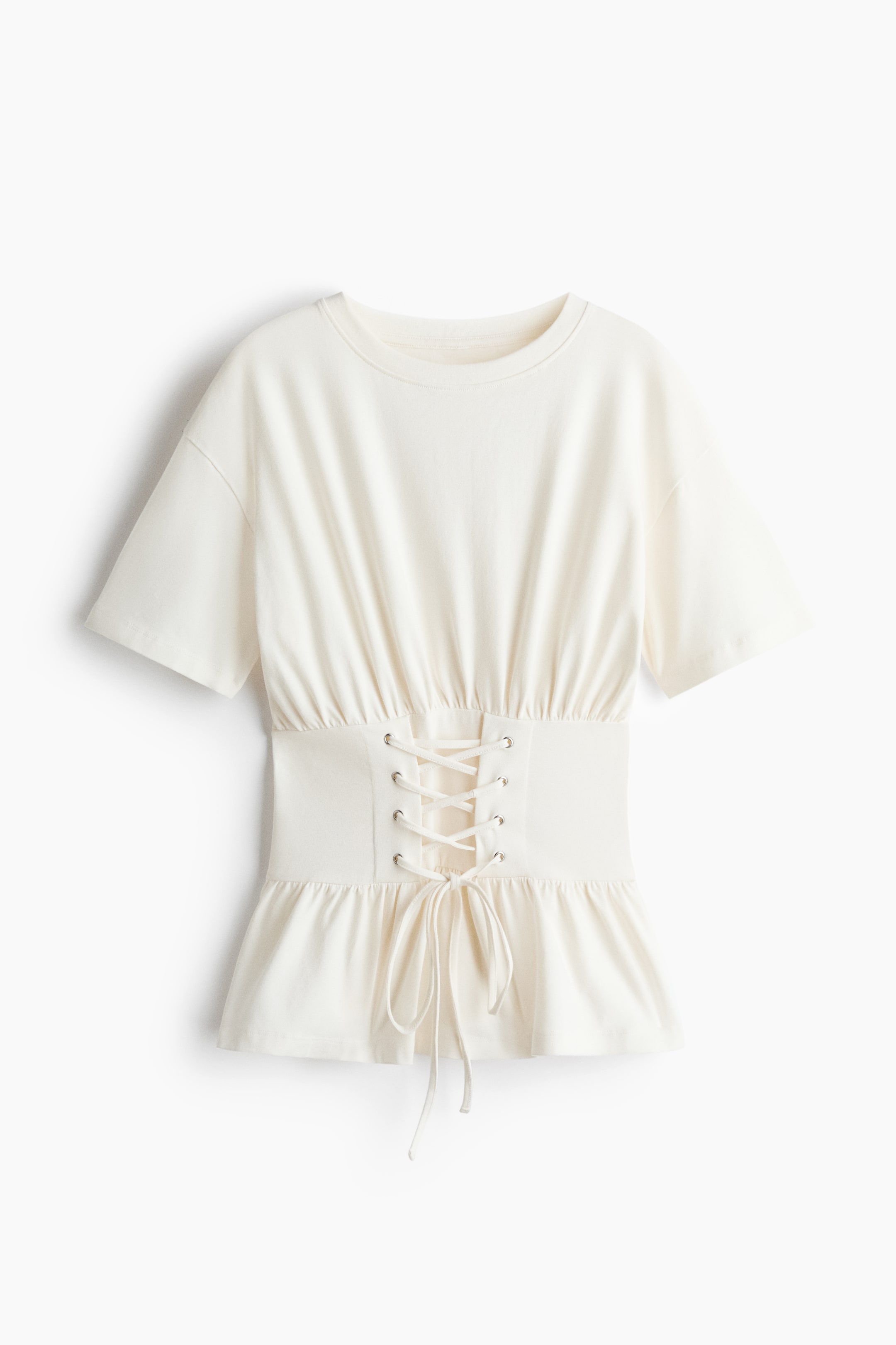 Agrandir l'image: Un t-shirt blanc cassé est présenté de face, avec un col rond, des manches courtes et une large ceinture style corset ajustée, agrémentée d'œillets ton argent et d'un laçage à nouer. Le tissu se fronce délicatement au-dessus de la ceinture et s'évase en dessous pour former un ourlet peplum volanté.
