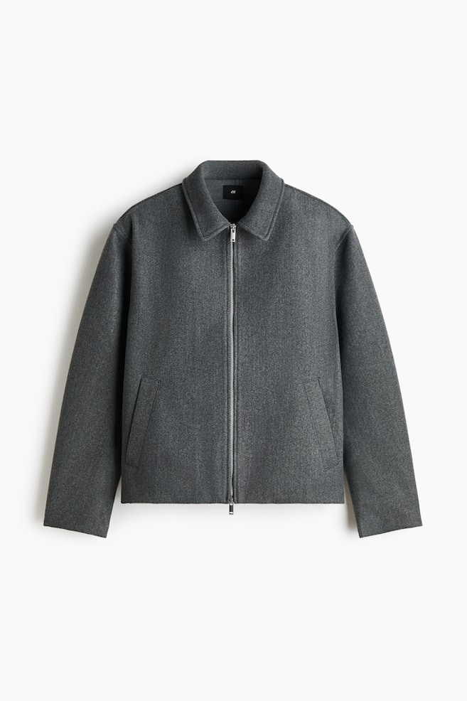 En overshirt i gråt filtet stof ses forfra med klassisk krave, lynlås foran i sølvfarvet metal og diagonale paspolerede lommer. Det langærmede beklædningsstykke fremstår med en struktureret, skarp silhuet og lige kant forneden. - 1