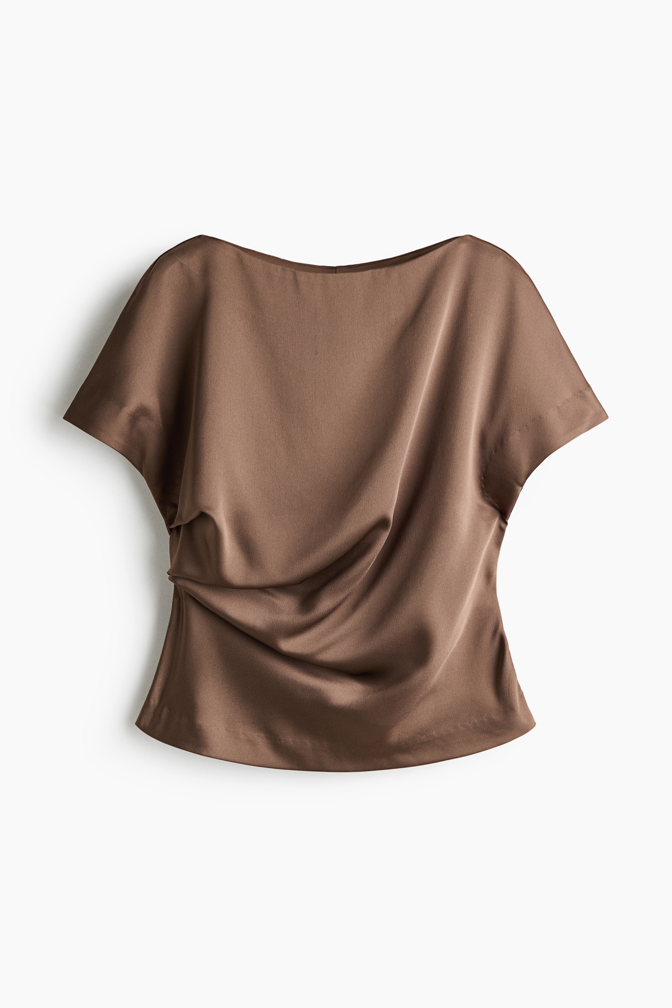 A brown satin blouse featuring a boat neckline, cap sleeves, and draped pleating at the waist is worn by the model. The blouse is styled with black trousers, black sunglasses, and silver statement earrings.