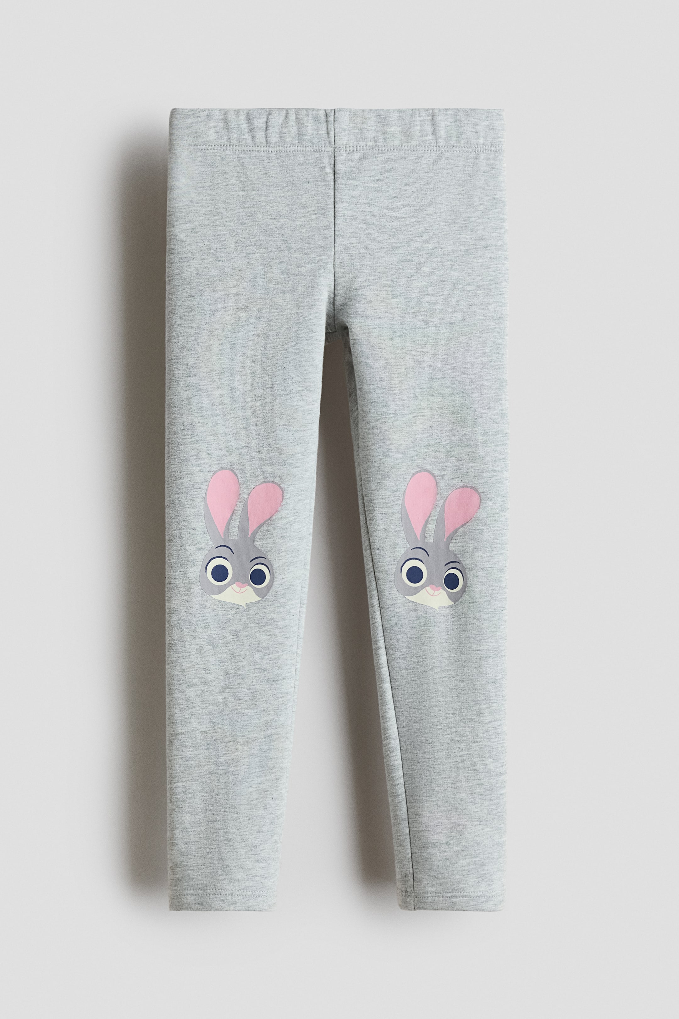 拡大画像を表示: ライトヘザーグレーのレギンスは、伸縮性のあるウエストバンドとフルレングスの脚を特徴としています。グレーの毛、ピンクの内耳、大きな青い目を持つ2つの漫画のウサギの顔が、膝の部分を飾っており、前面から見ることができます。