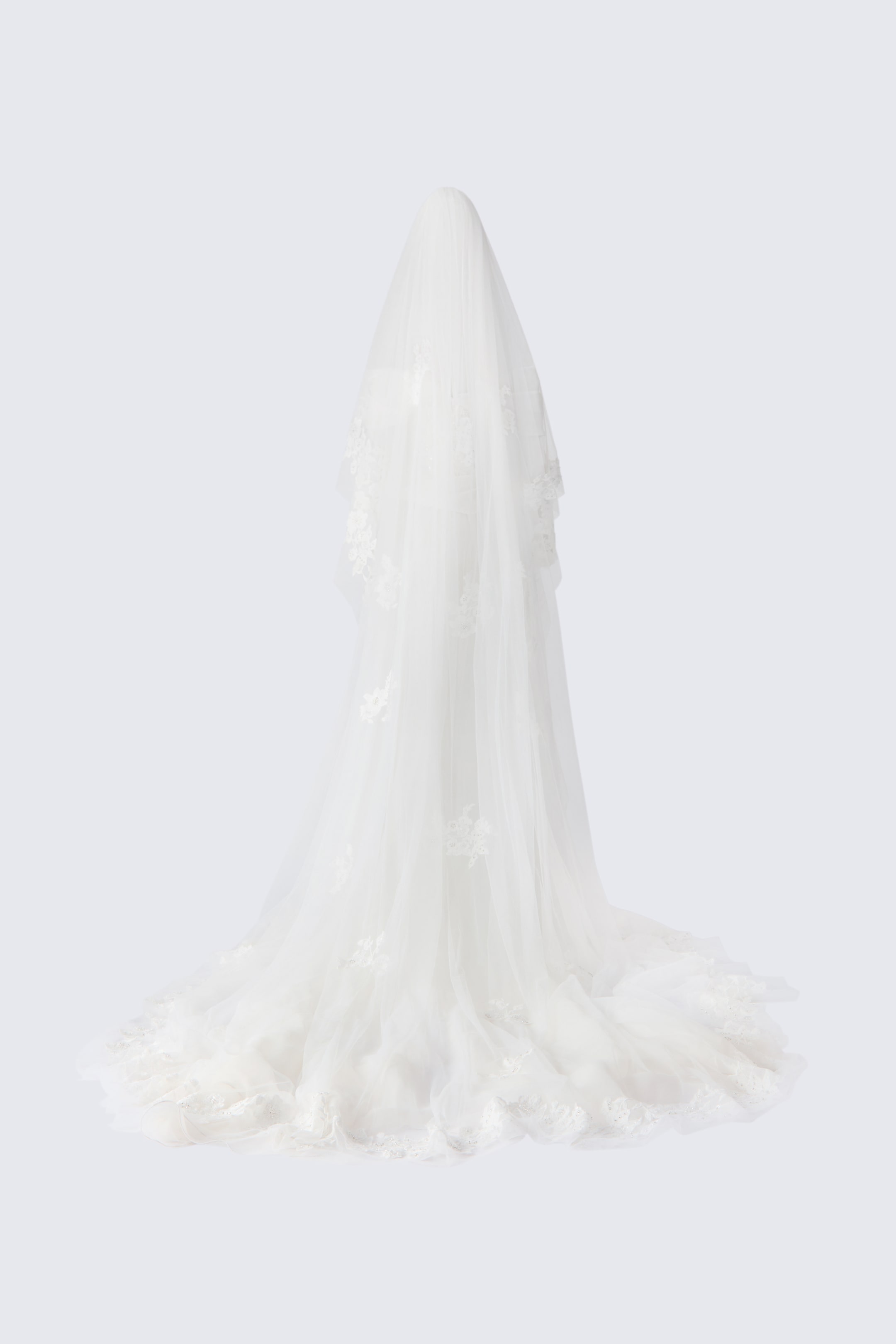 View larger image: The Floral Detail Wedding Veil drapes downward from a central point and pools on the floor, shown from the rear to highlight its full length. The sheer tulle veil features delicate floral lace appliqués scattered along the fabric and trim.