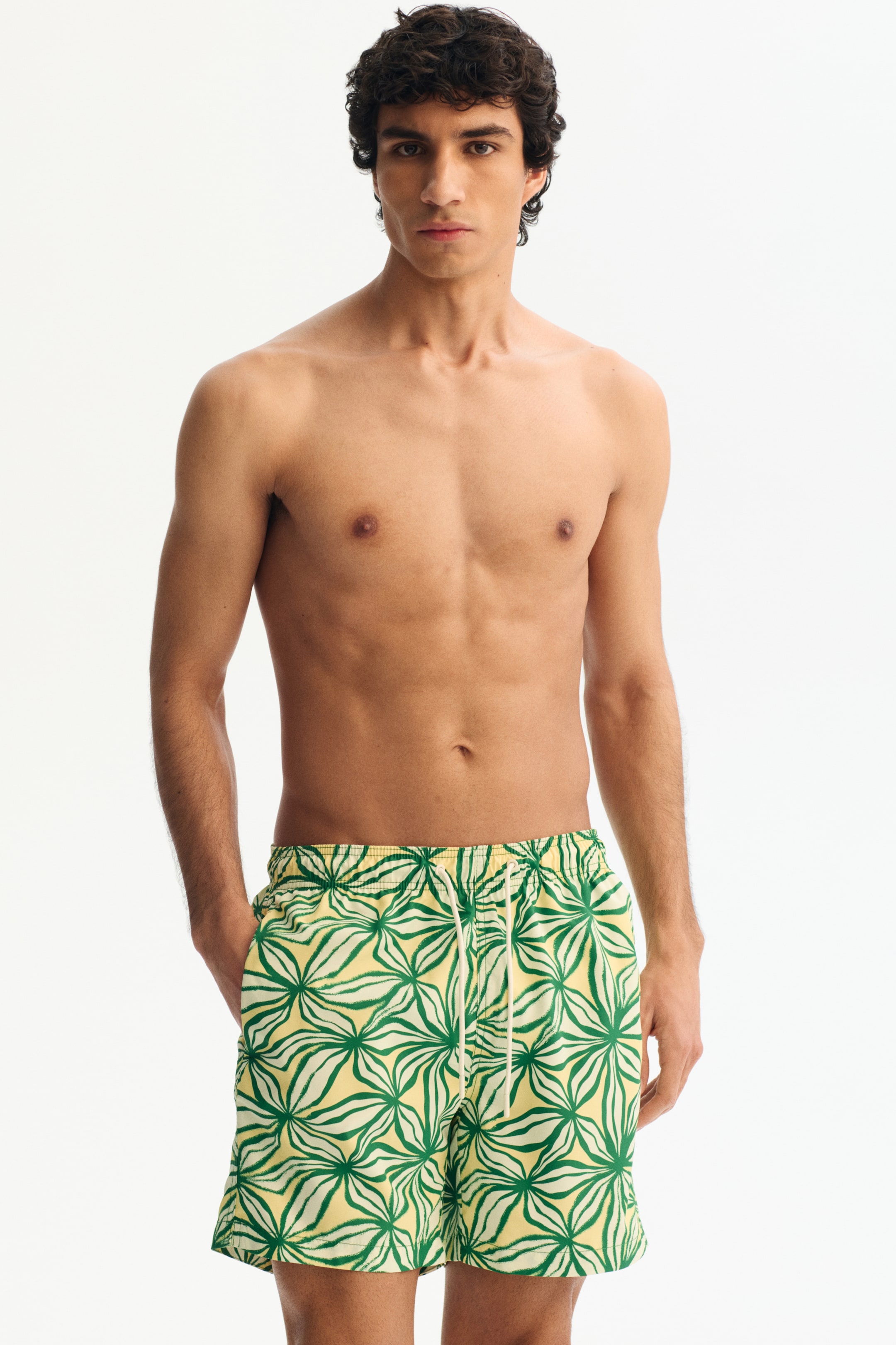 Agrandir l'image: Les shorts de bain présentent une taille élastiquée avec un cordon de serrage blanc cassé, un fond jaune avec un motif floral abstrait vert, et une coupe décontractée mi-cuisse.