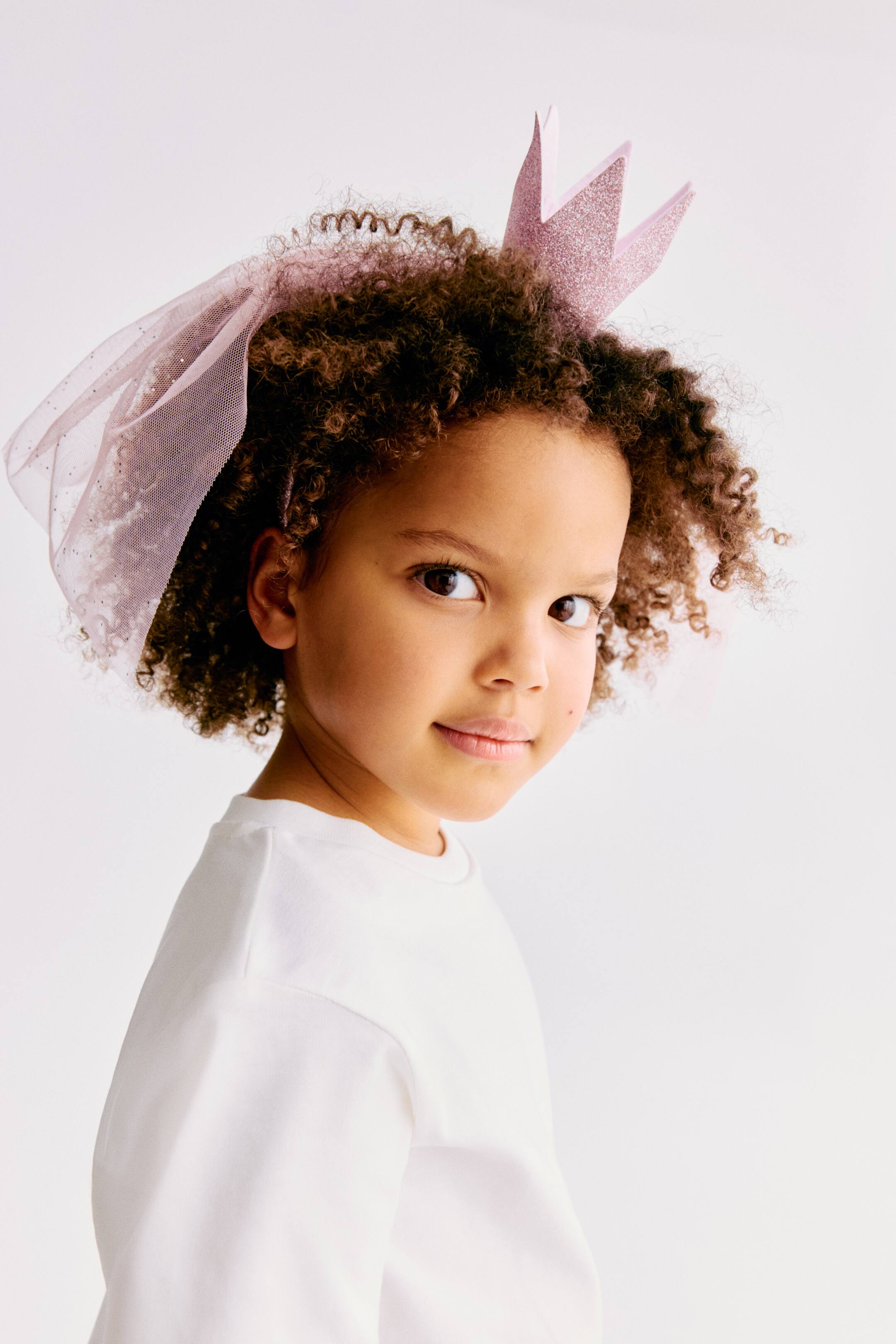 Ampliar la imagen: Una corona de brillo rosa, con puntas puntiagudas, está siendo usada, con un velo de tul transparente rosa brillante que fluye desde su parte trasera.