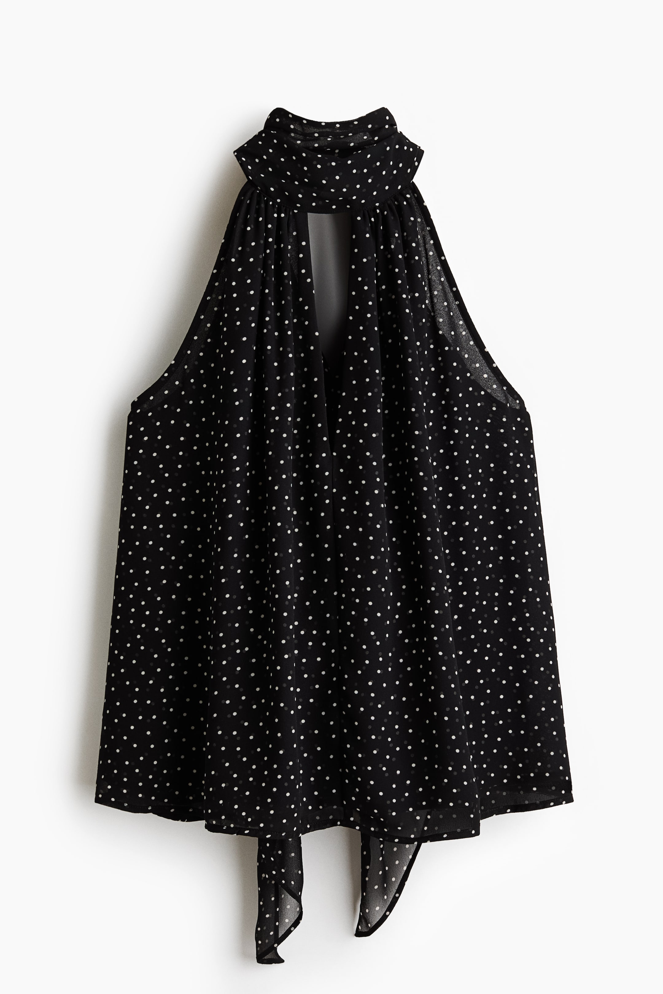 View larger image: A black polka-dot sleeveless top is displayed front-facing. It features a gathered high neckline with a keyhole cut-out, wide armholes, an asymmetrical hem, and two fabric ties at the front.
