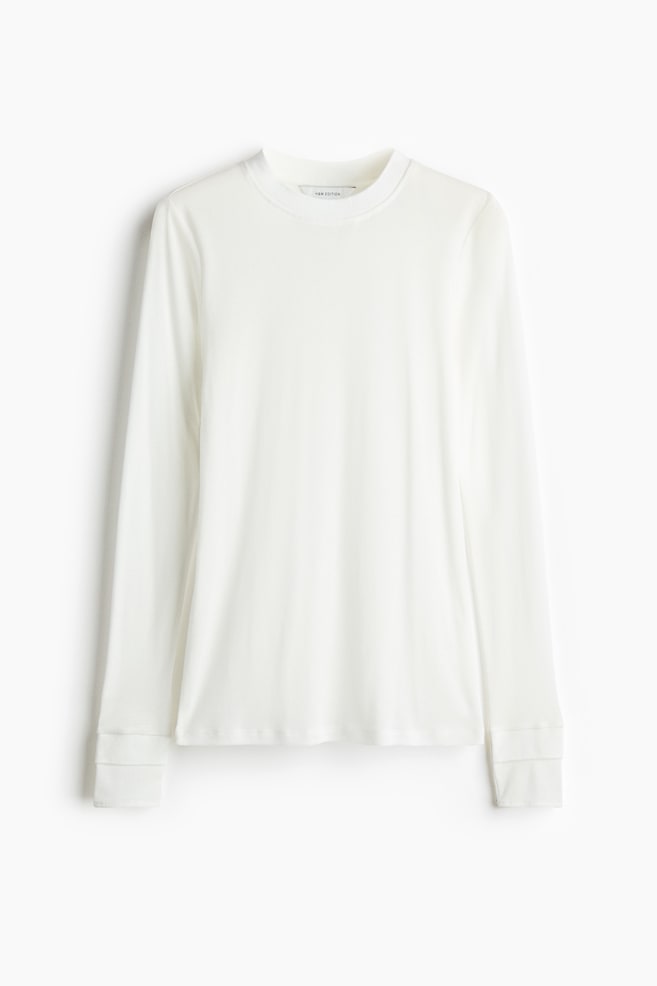 A white long-sleeved top in cotton jersey is hanging front-facing, showing a round, rib-trimmed neckline. The long sleeves feature double-layered panels at the cuffs. - 1