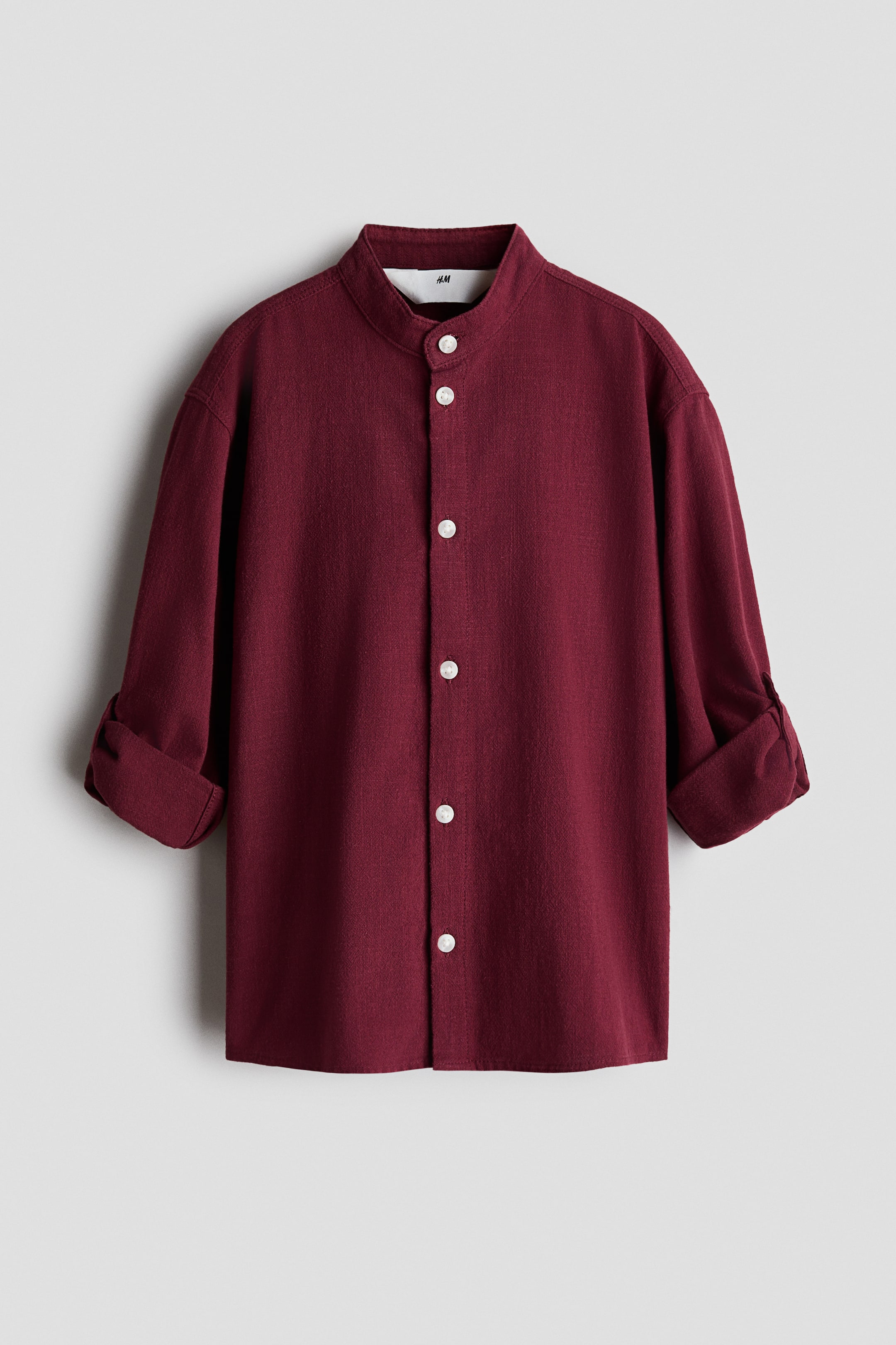 View larger image: A burgundy shirt in a soft, airy weave is shown from the front, featuring a band collar and a front button closure with contrasting white buttons. The long sleeves are rolled up to the elbows, highlighting its casual, relaxed design.