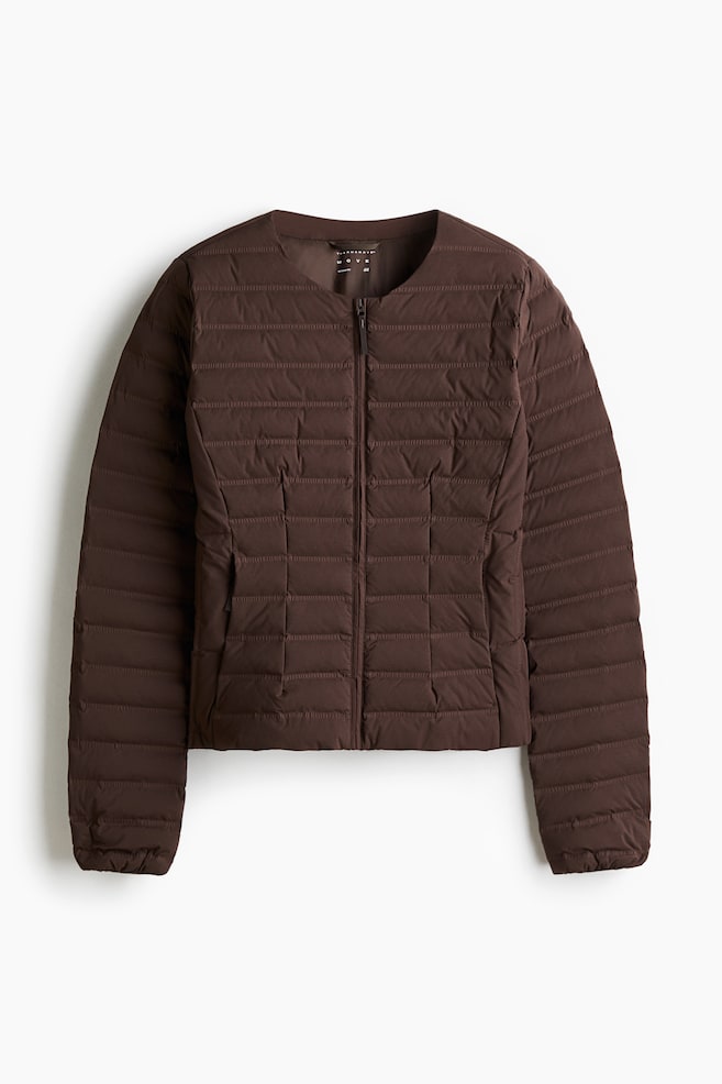 A dark brown insulated jacket is presenting from the front, featuring a collarless, round neckline, a full-length black zipper, and two subtle vertical zippered pockets near the waist. The jacket is showcasing horizontal quilting on the sleeves and upper body, transitioning to square quilting around the waist, with a small 'THERMOMOVE' label visible at the back of the neck. - 1