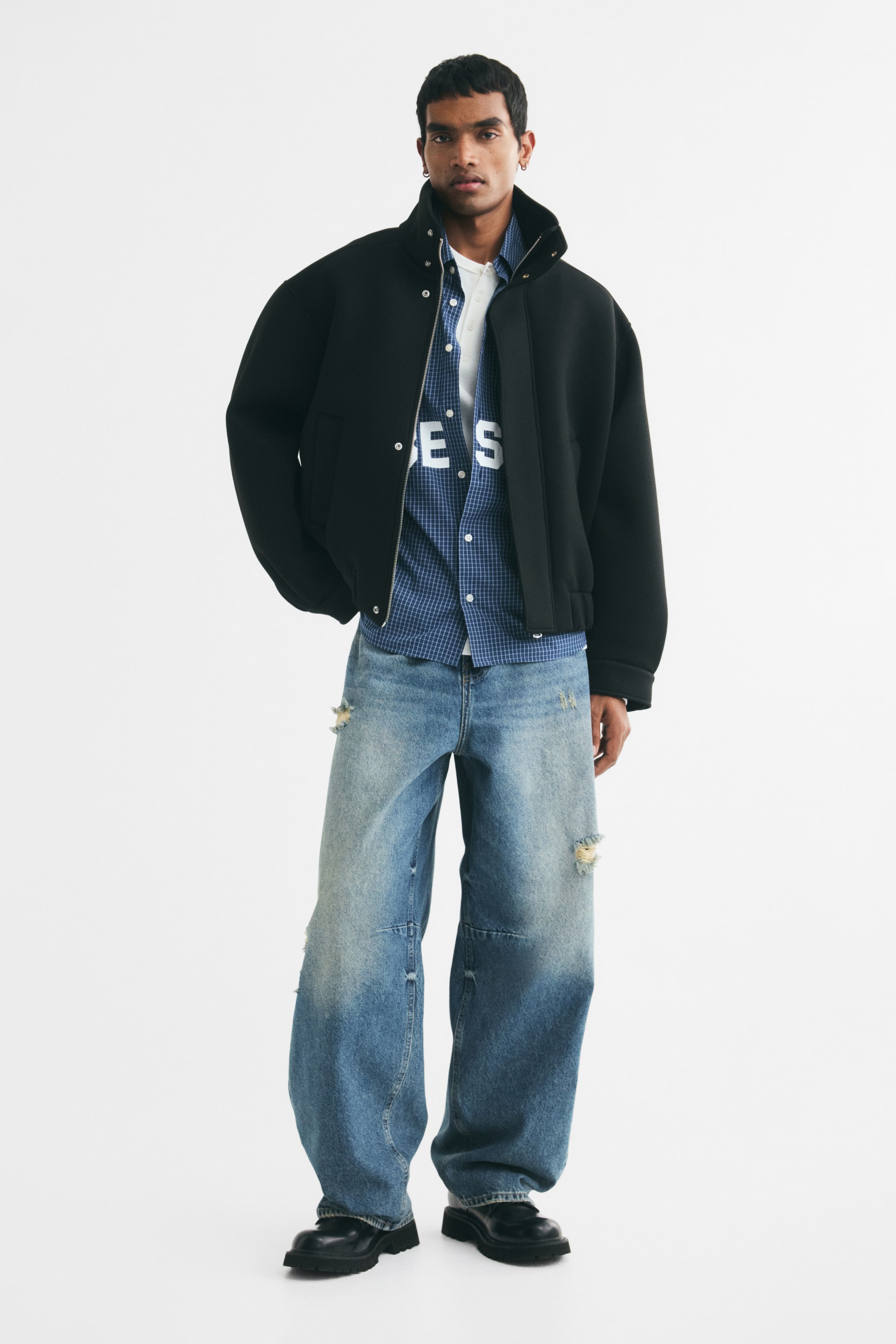 Grotere afbeelding bekijken: 5-pocketjeans in stug blauw katoenen denim met versleten details worden gedragen door het model. De jeans heeft barrel legs met een baggy fit van zitvlak tot zoom, waardoor er veel ruimte is rond het hele been, en een regular waist met een knoopsluiting.