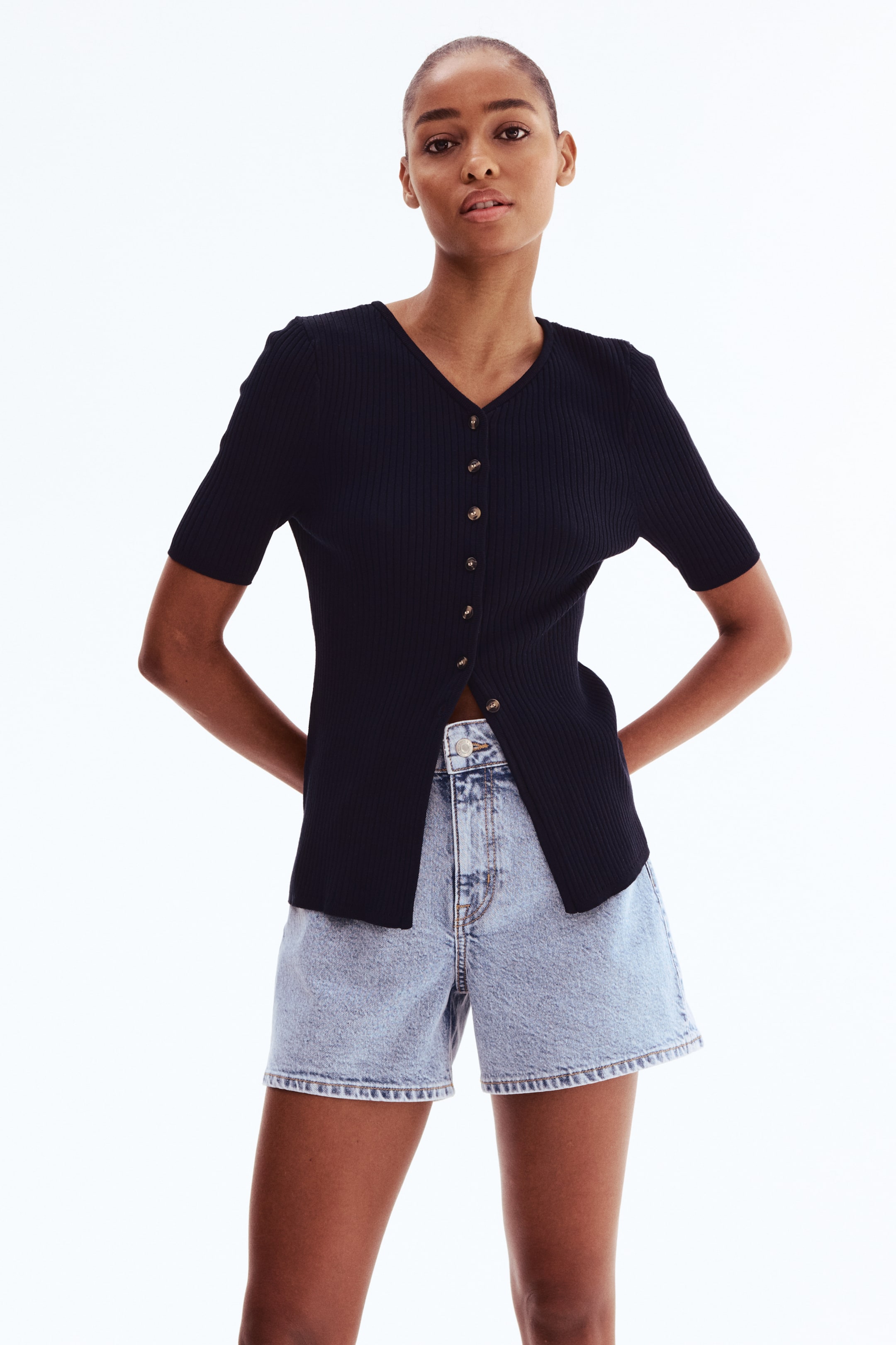 View larger image: A black ribbed knit top features a V-neckline, short sleeves, and a button-front closure with small, light-colored buttons. The lower front of the top is unbuttoned.
