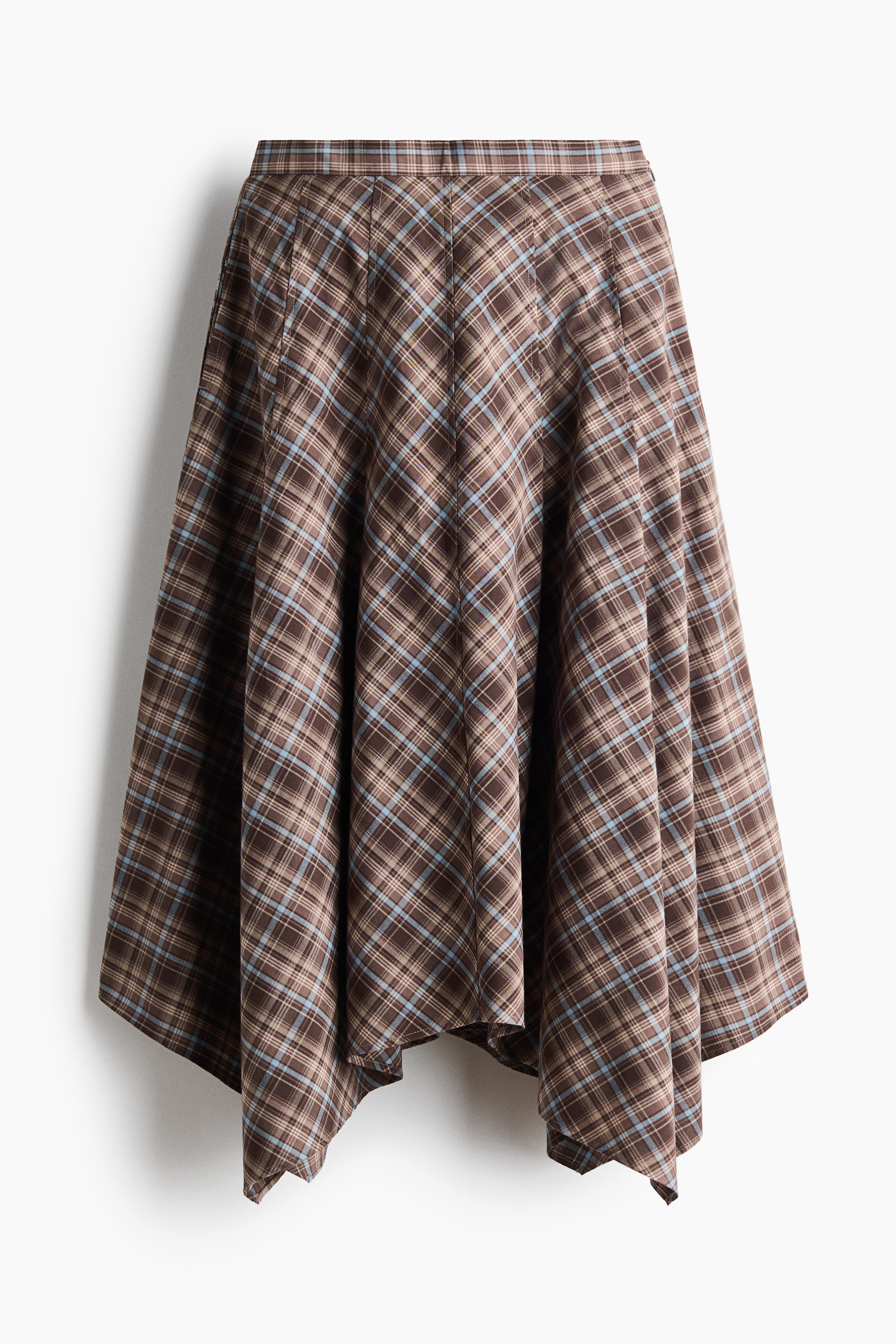 A blue-and-white plaid button-up shirt with a wraparound waist tie and a brown plaid asymmetrical skirt are worn by the model. The outfit is styled with a dark patterned scarf draped over one shoulder and knee-high dark leather boots.