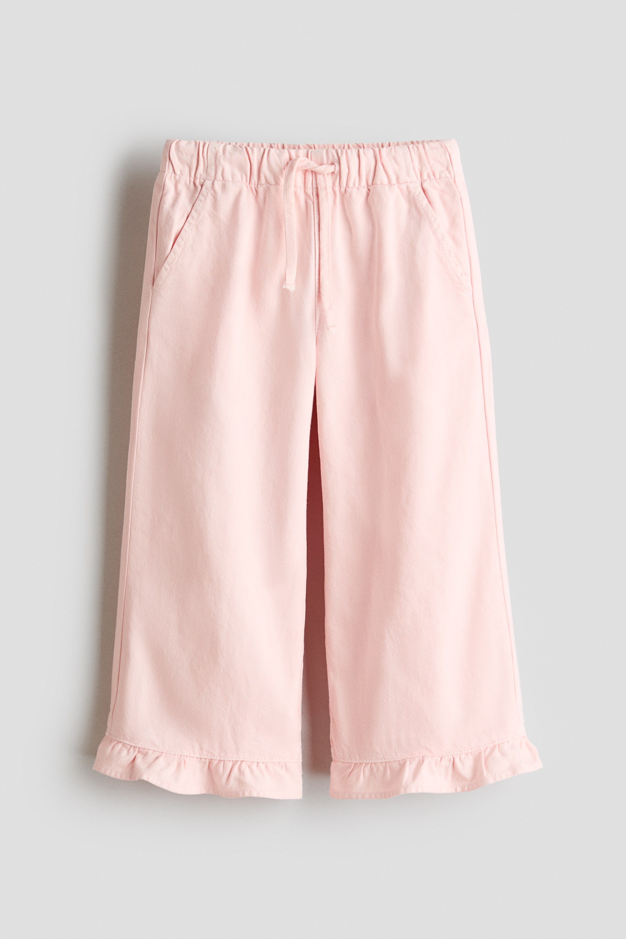 View larger image: Loose-fit pink trousers crafted from a breezy cotton weave, showcasing an elasticated drawstring waist, diagonal side pockets, wide legs, and frill-trimmed hems.