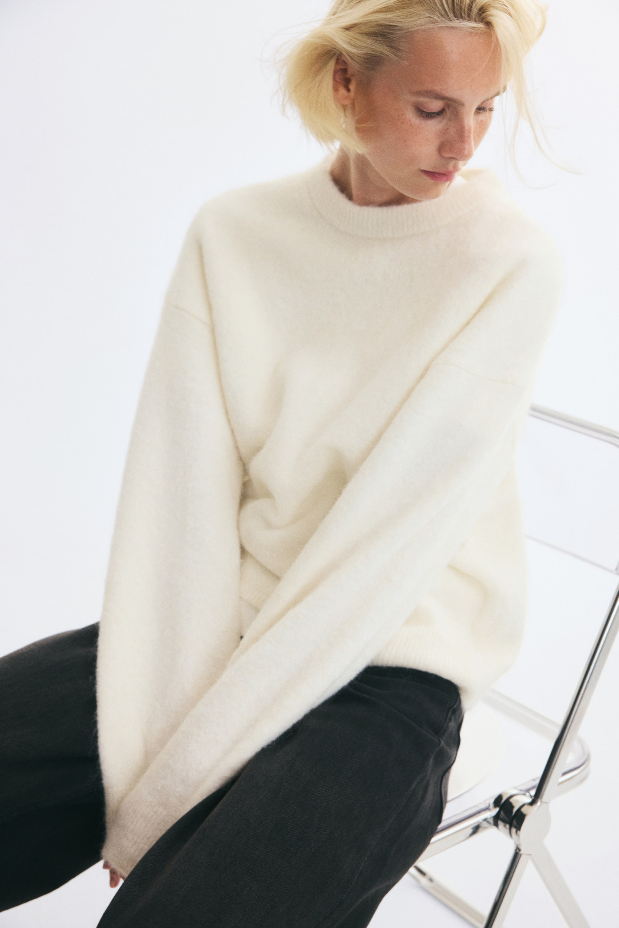 View larger image: An off-white sweater in a soft knit is worn by the model, featuring a round rib-trimmed neckline, dropped shoulders and long sleeves with ribbed cuffs. The sweater is styled with black trousers.