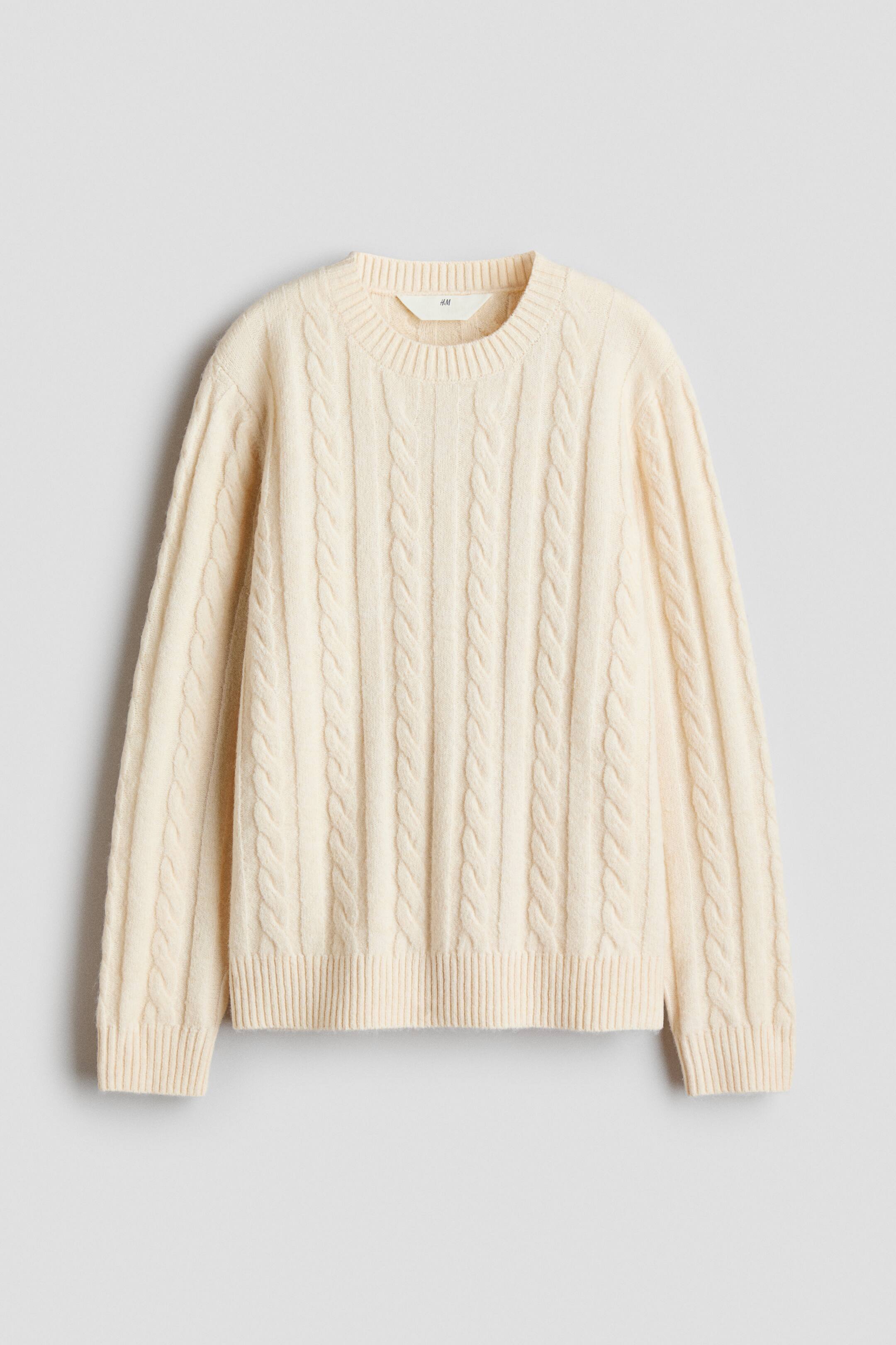 Agrandir l'image: Un pull en maille torsadée de couleur crème est présenté de face, mettant en valeur des motifs torsadés verticaux le long du corps et des manches. Le modèle présente un col ras du cou côtelé, des poignets côtelés et un ourlet côtelé.